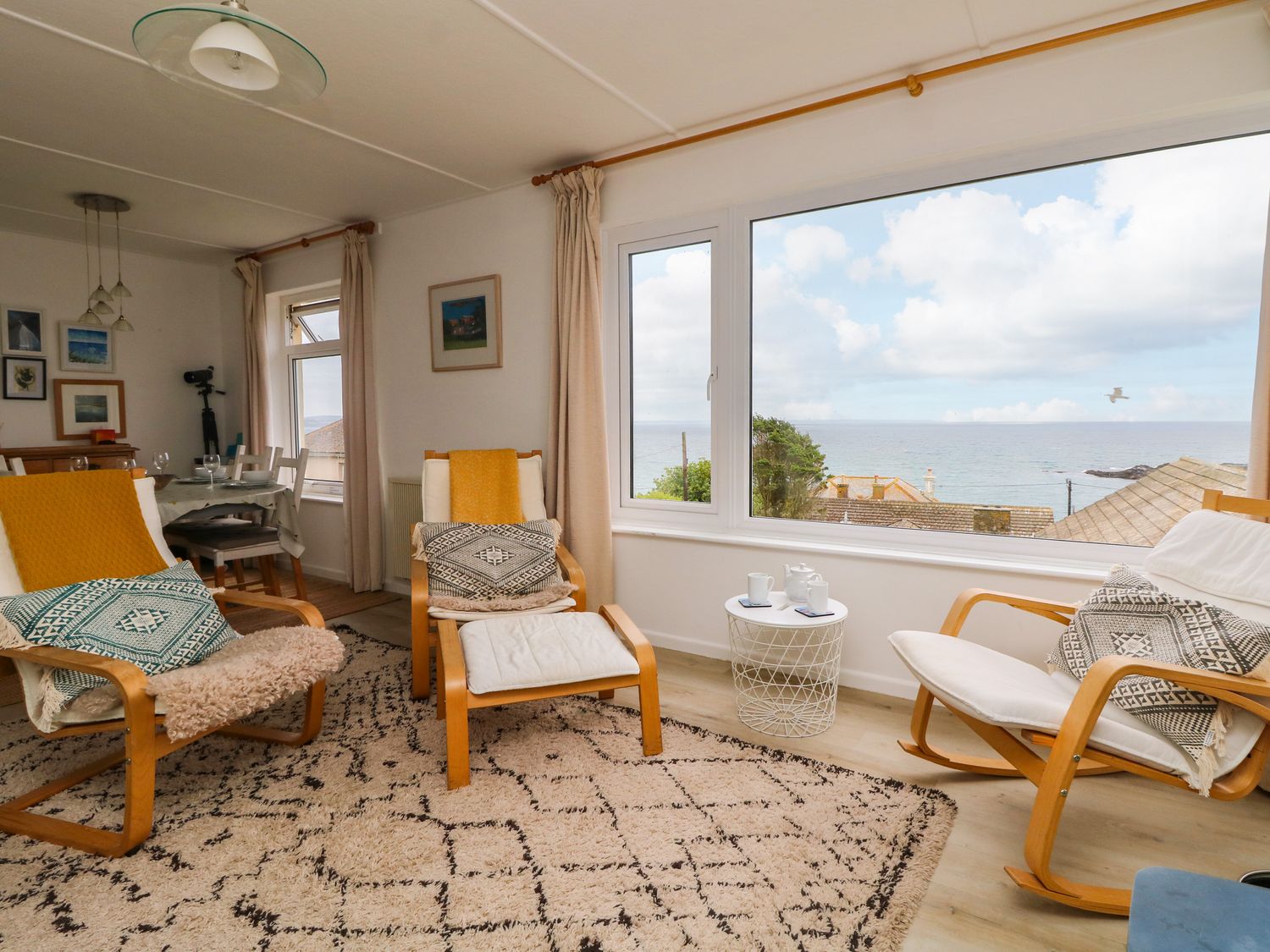 A living room with chairs and a small table near large windows overlooking the sea at Wootton Gray in Mousehole