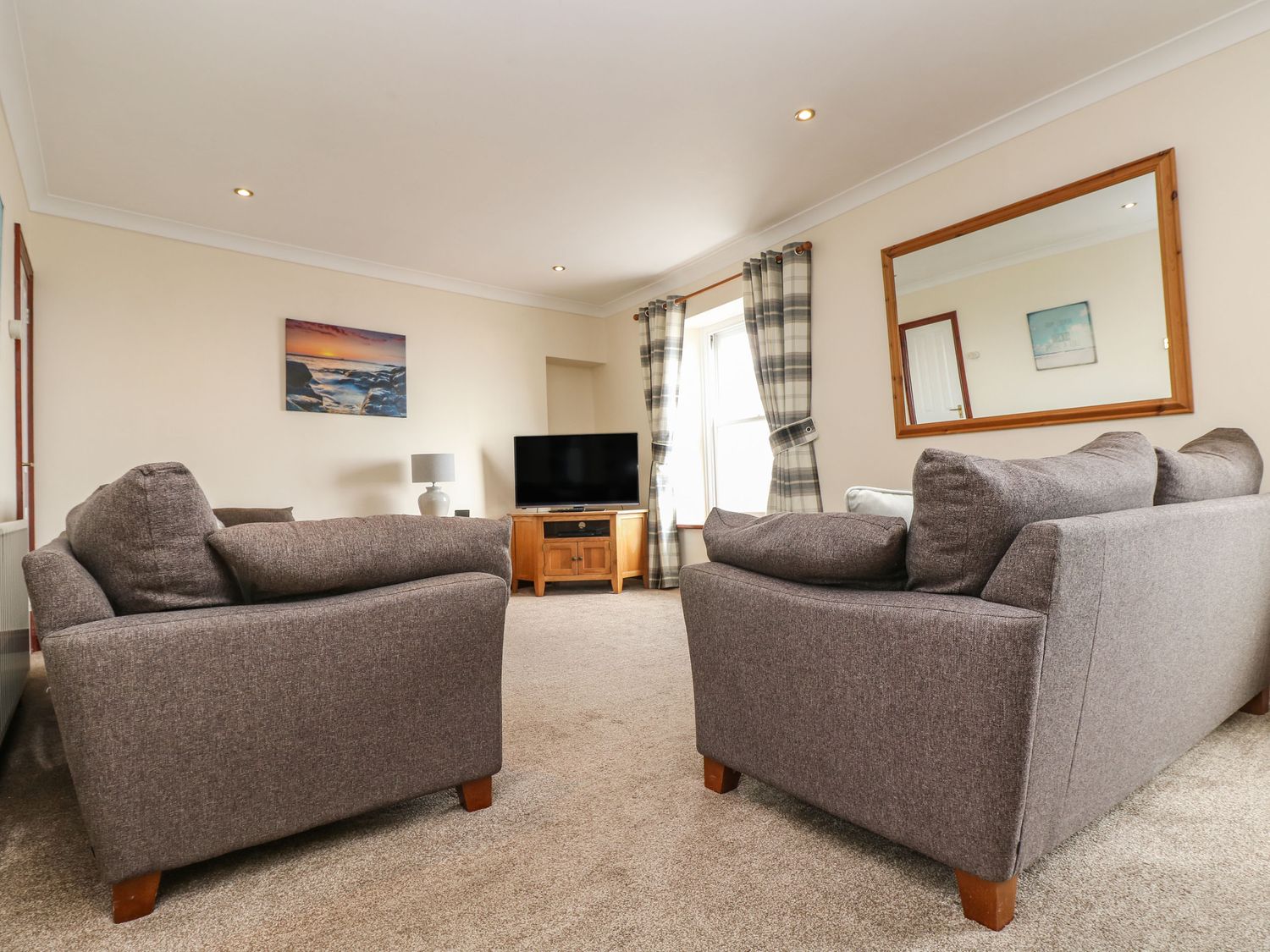 A living room with two grey sofas a TV on a wooden cabinet a lamp curtains and a large mirror at Jubilee Cottage in Penzance