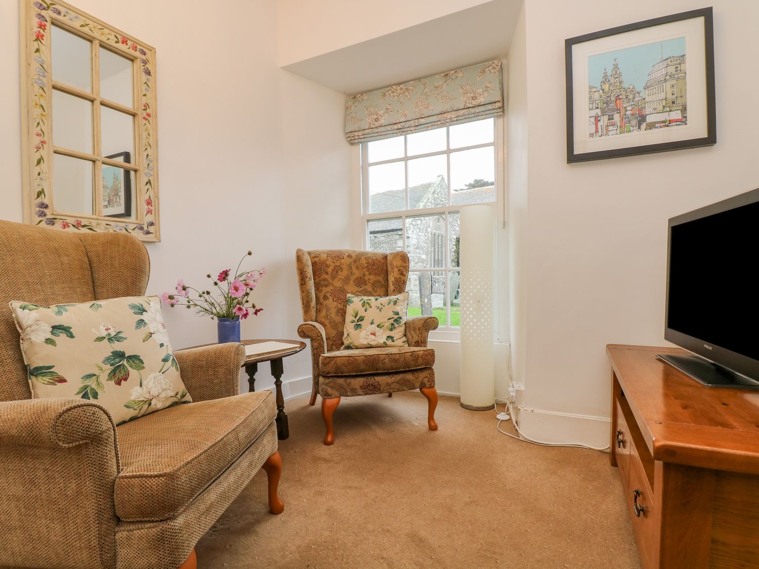 A sitting room with two armchairs a television on a wooden stand a window and a mirror on the wall at Eden House Wing in St Keverne