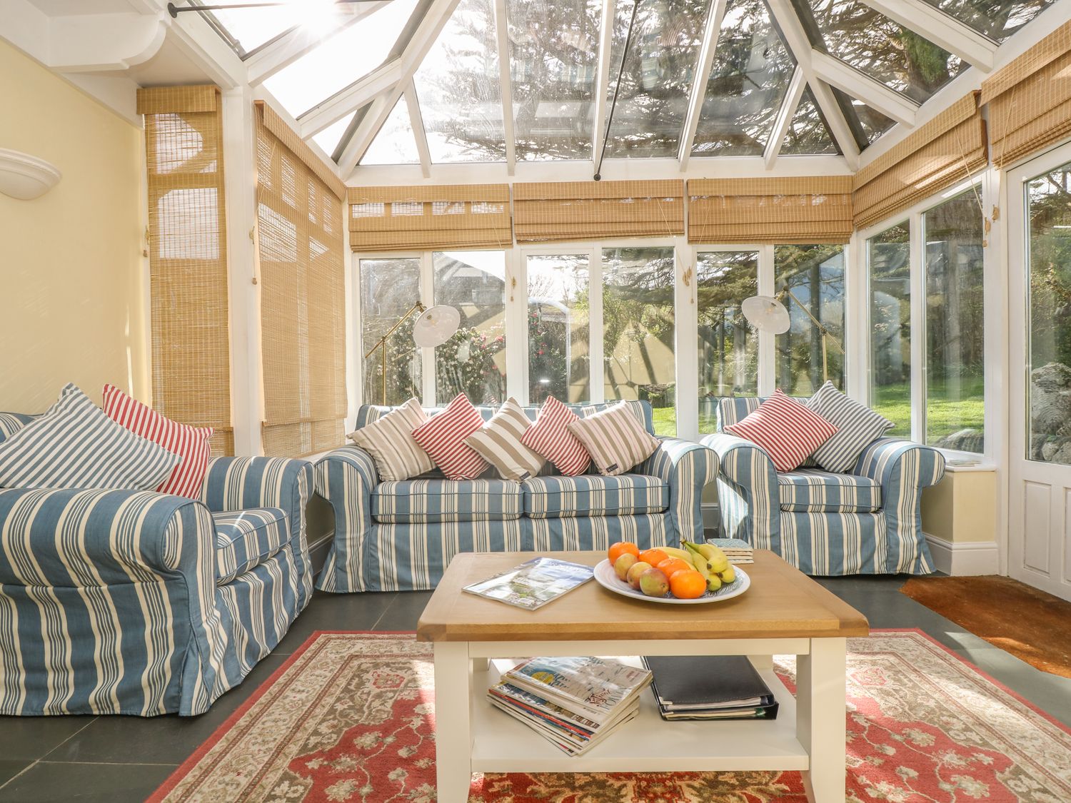 A sunroom with striped sofas and a coffee table with fruit at Boskednan Wartha in Penzance