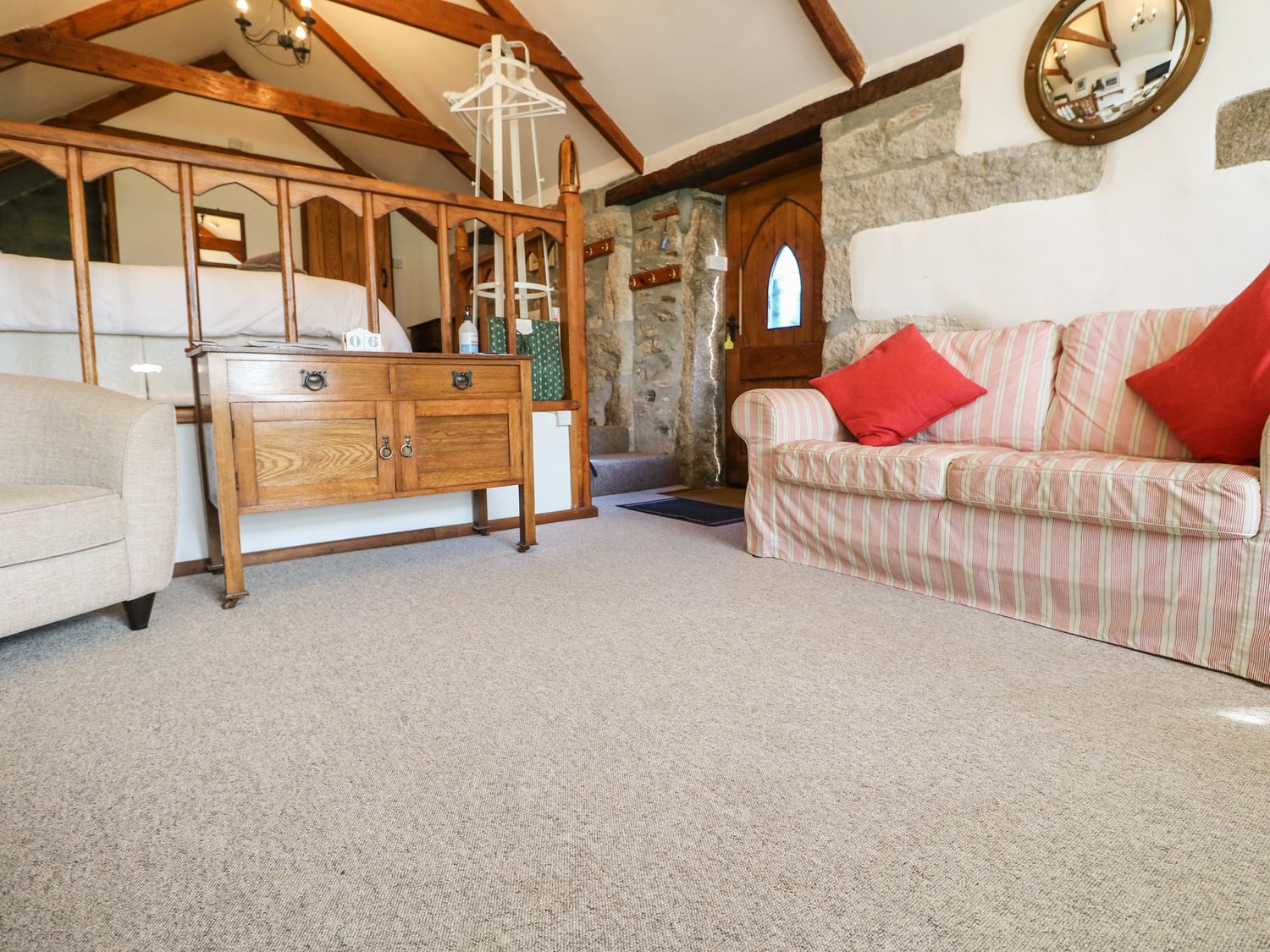 A living room with a striped sofa with red cushions wooden furniture and a stone wall at Trevenning Chapel Near Port Isaac