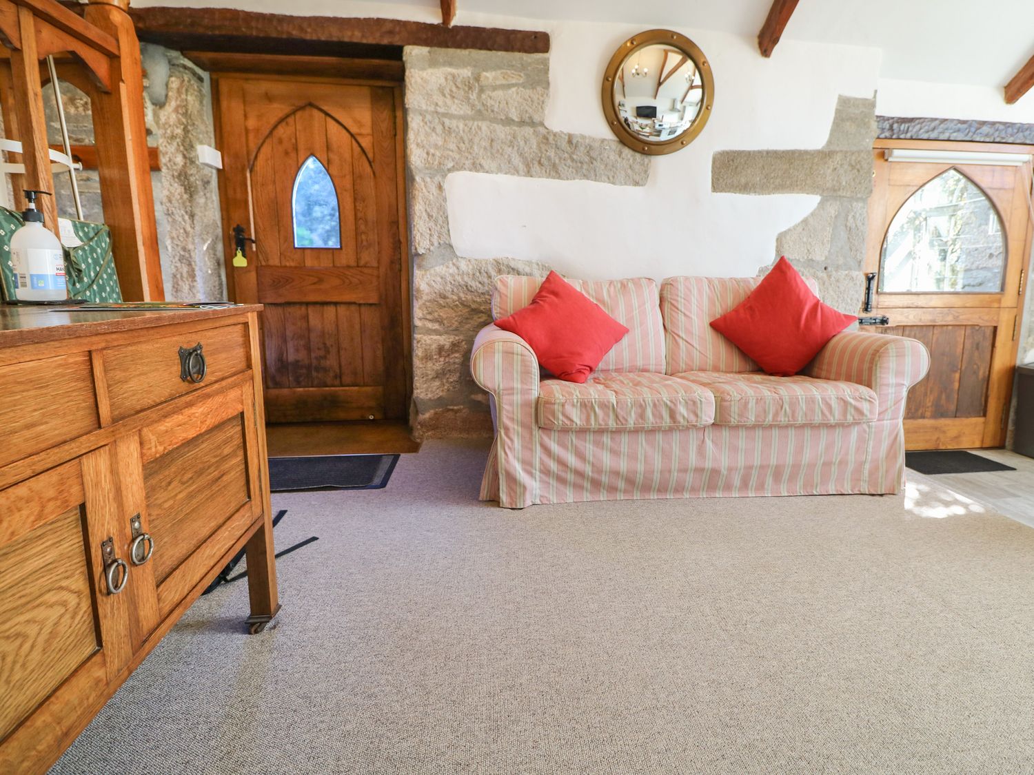 A sitting area with a striped sofa with red cushions wooden cabinets and wooden doors in a room at Trevenning Chapel Near Port Isaac