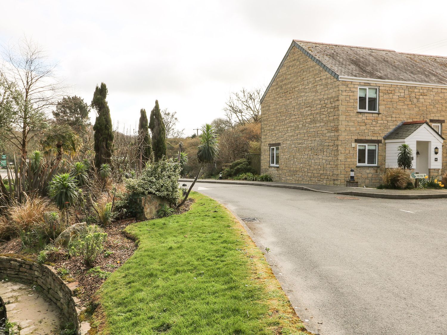 A stone house beside a curved road with grass and shrubs on the side at Heather's Cottage in Falmouth