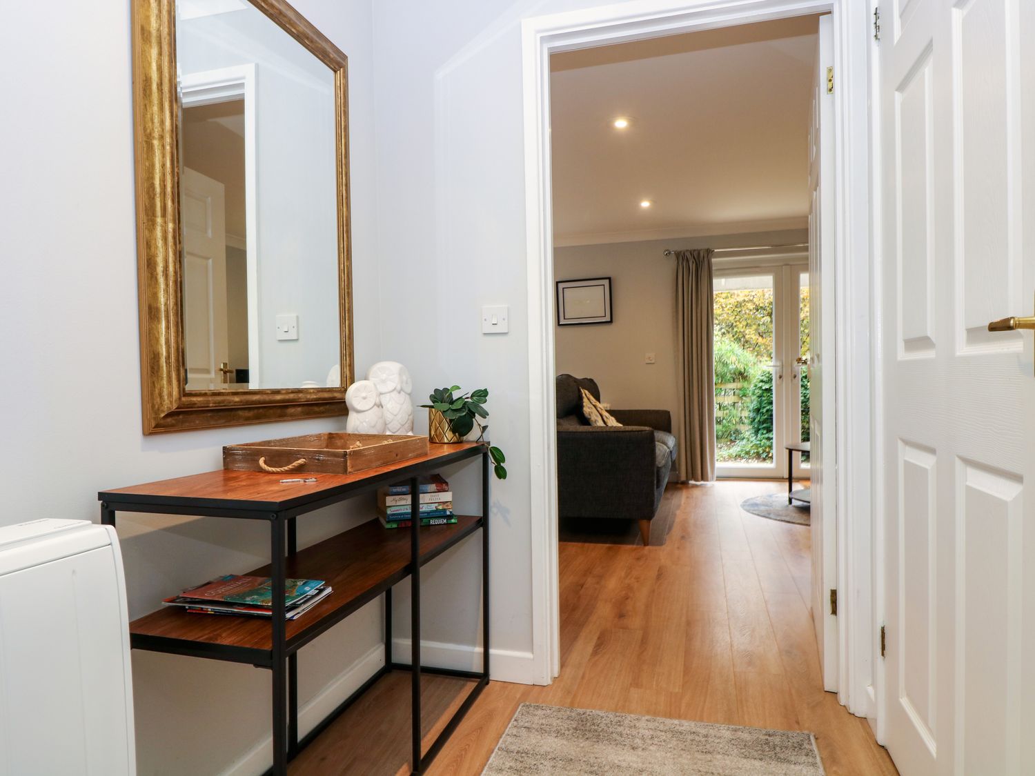 A hallway with a wooden console table holding books, decorative items, and a large mirror with a gold frame at Heather's Cottage in Falmouth
