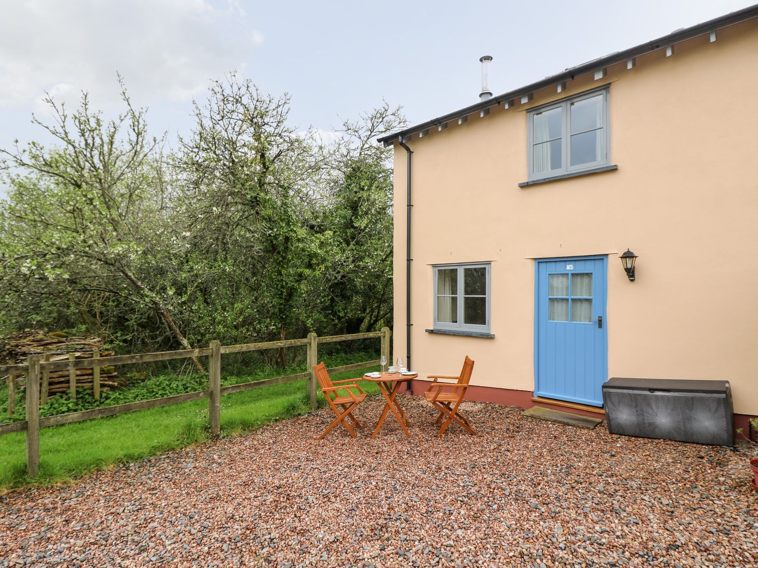 An outdoor area with a small table and two chairs next to a house with a blue door and windows at Plum Cottage in Colebrooke near Crediton
