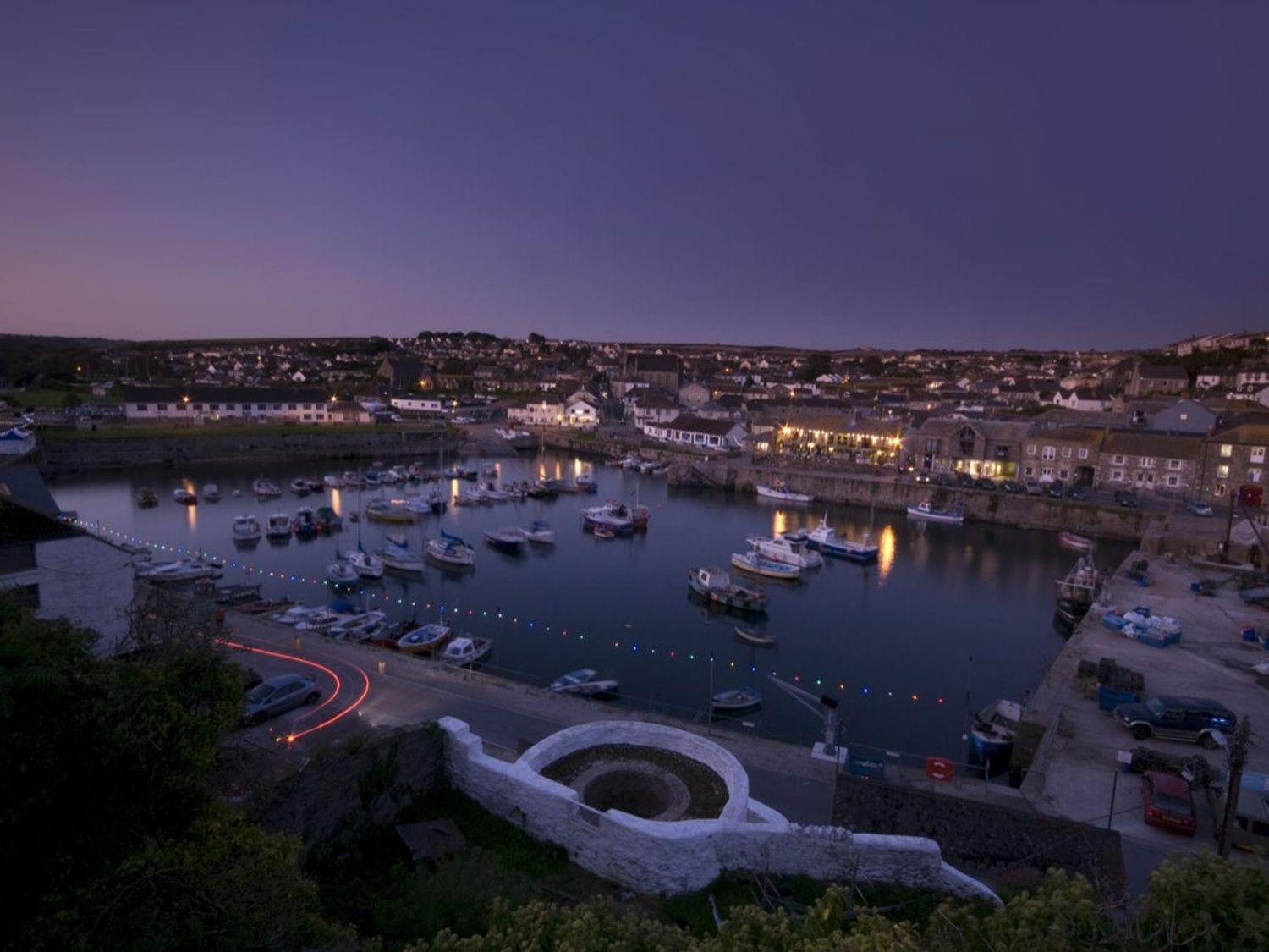 A harbor with boats docked and lights reflecting on the water during dusk at Rosa Cottage in Porthleven