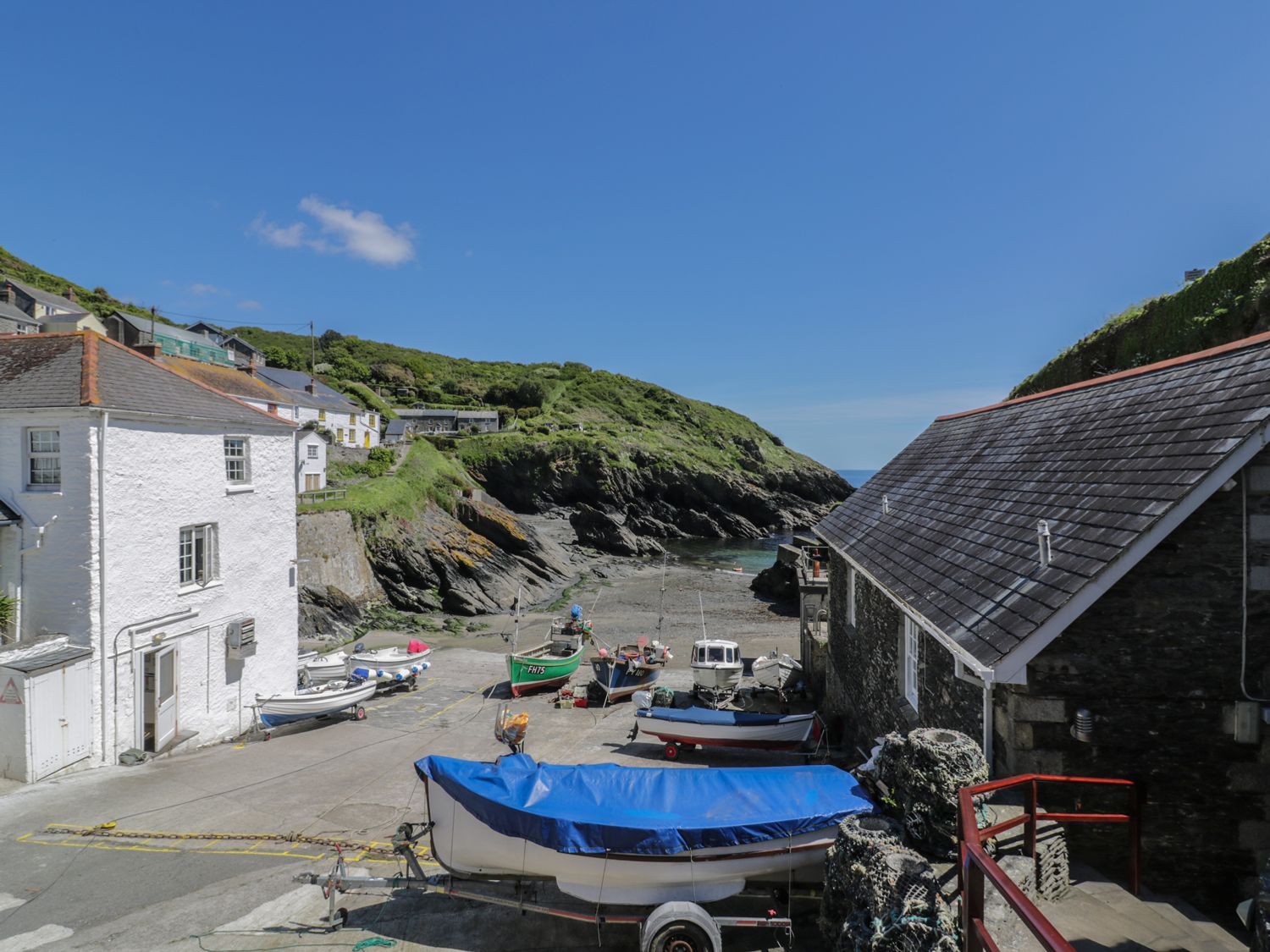 A small harbor with boats on a dock surrounded by buildings and green hills at Kerbenetty Harbour Cottage in Portloe