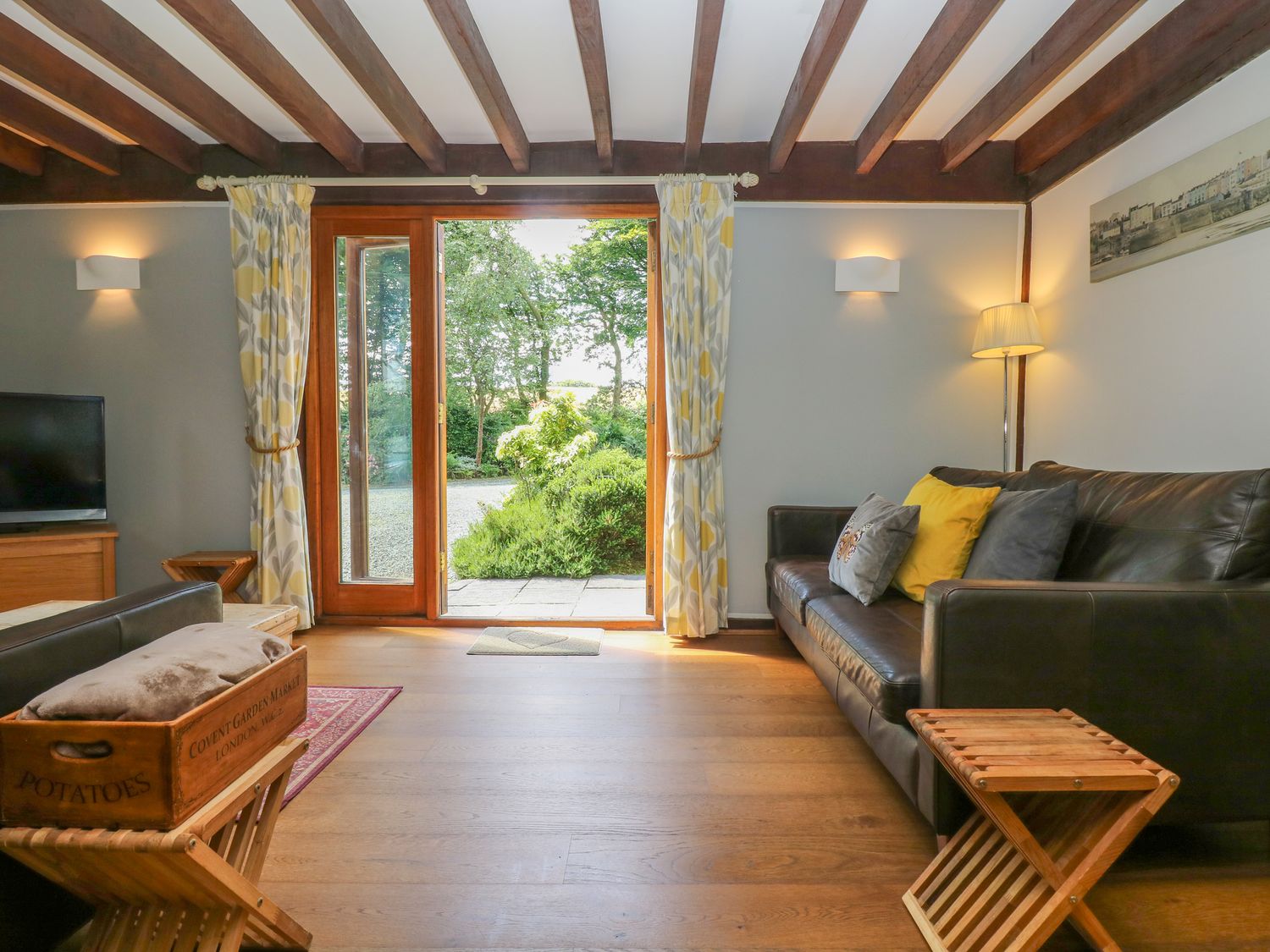 A living room with a brown leather sofa wooden beams and glass doors opening to a garden at Oaklands Near Boscastle