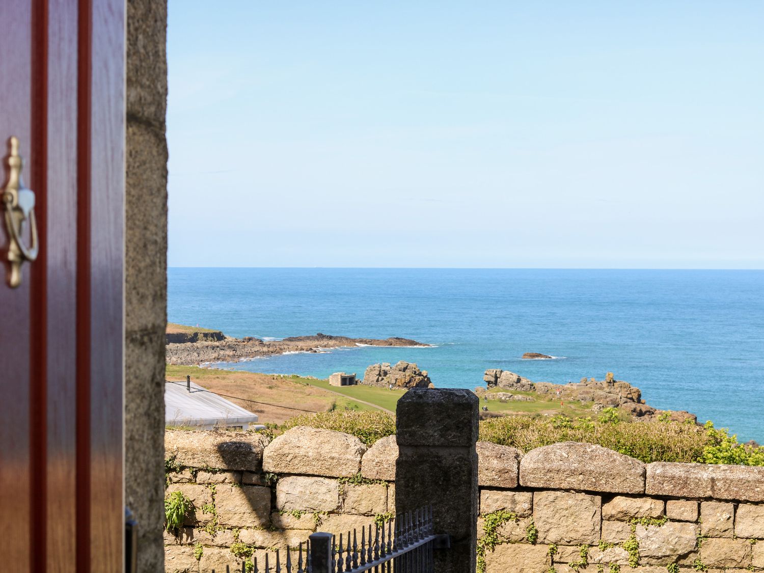 A view of the ocean and rocky coastline beyond a stone wall and an open red door at Porthmeor Beach House in St Ives