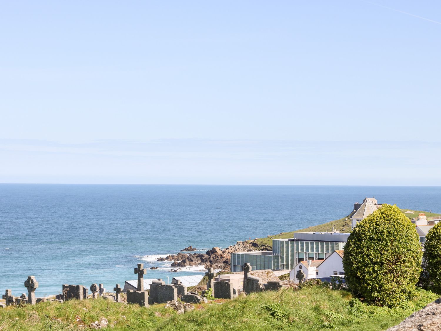A cemetery by the sea with gravestones and a modern building near the coastline at Porthmeor Beach House in St Ives