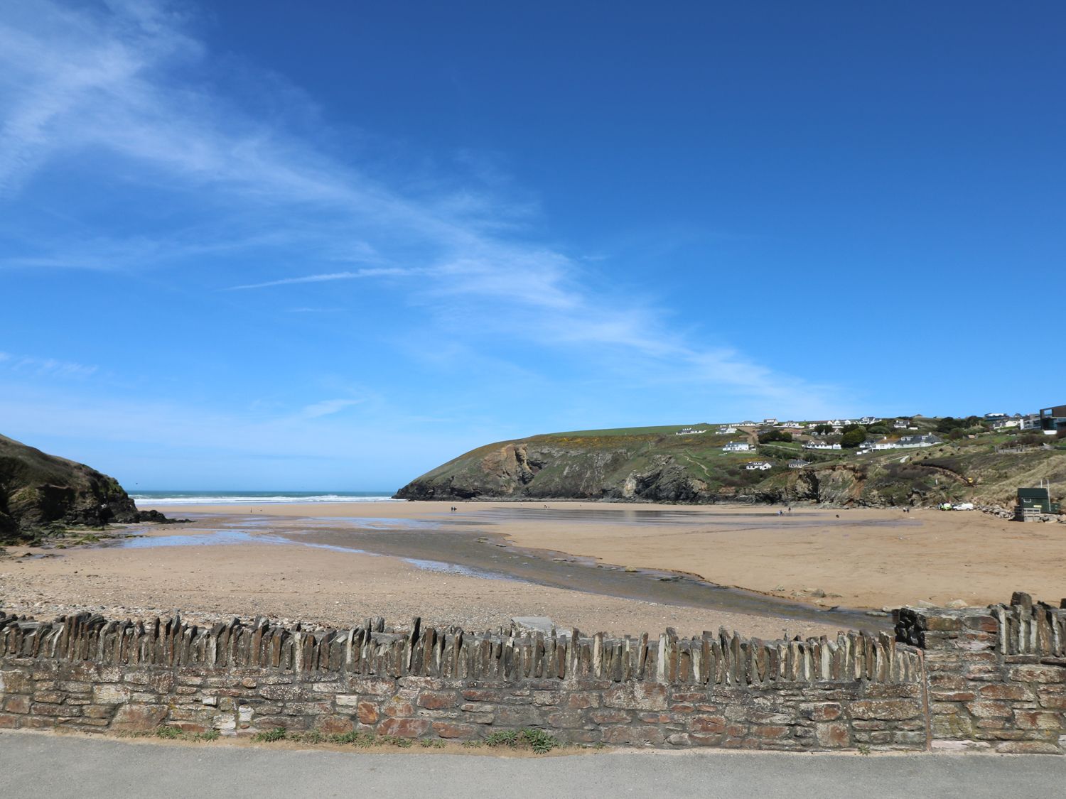 A beach with sand and a stone wall in the foreground and cliffs with houses in the background at Seaport Lodge in Mawgan Porth