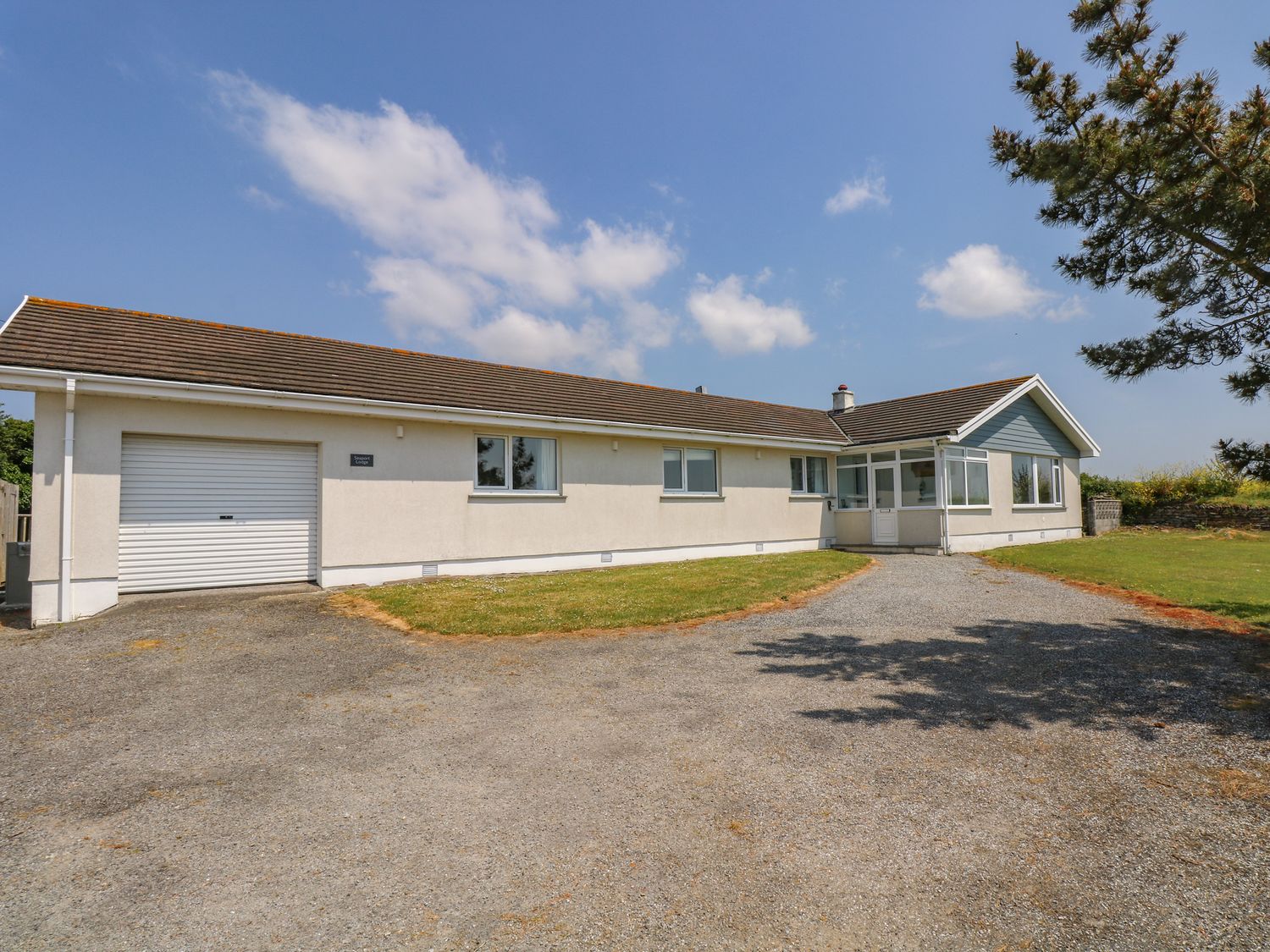 A single story house with garage and driveway surrounded by grass and trees at Seaport Lodge in Mawgan Porth