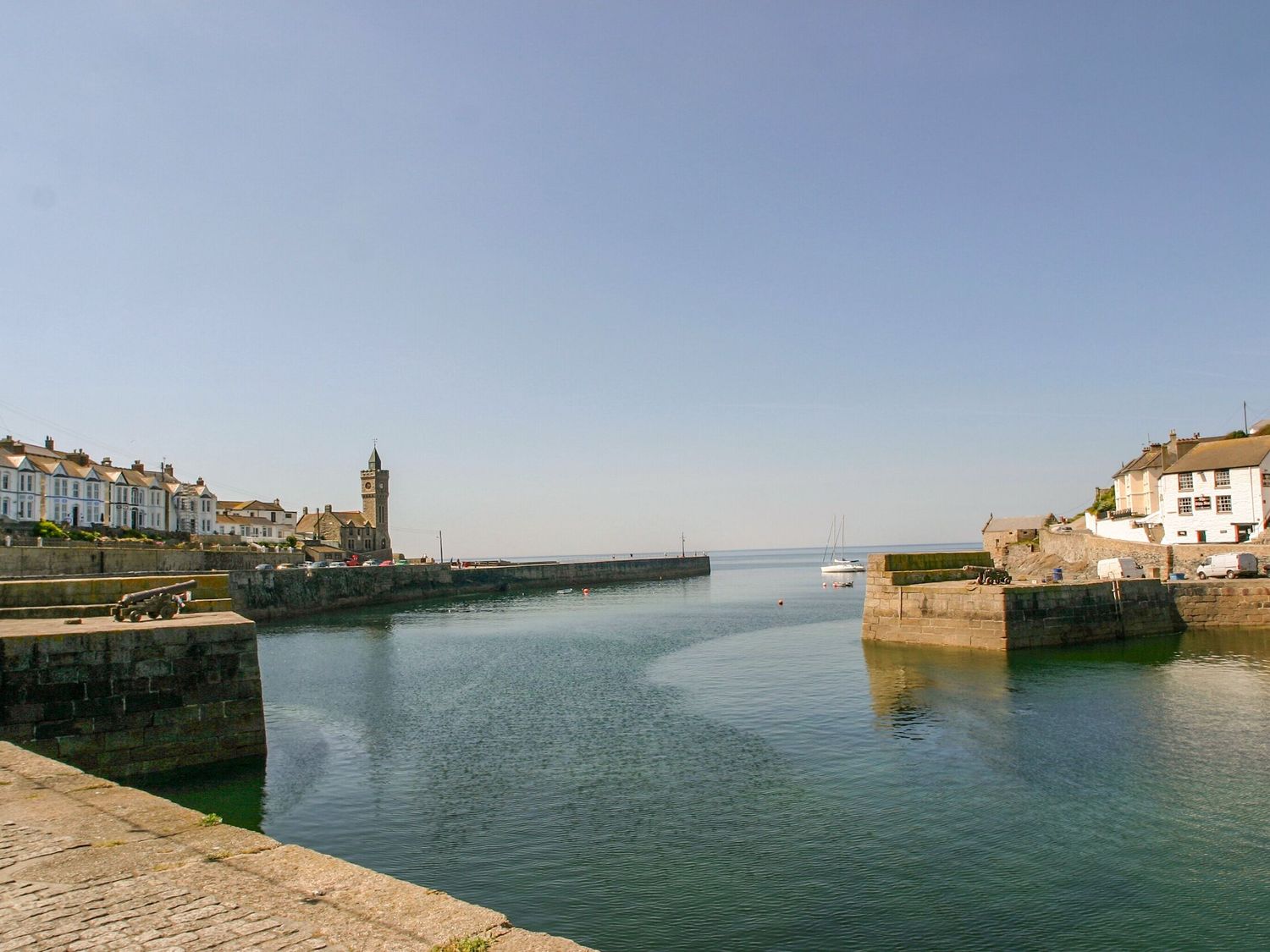A harbor with stone walls and boats on calm water at Little Tregarrick in Helston