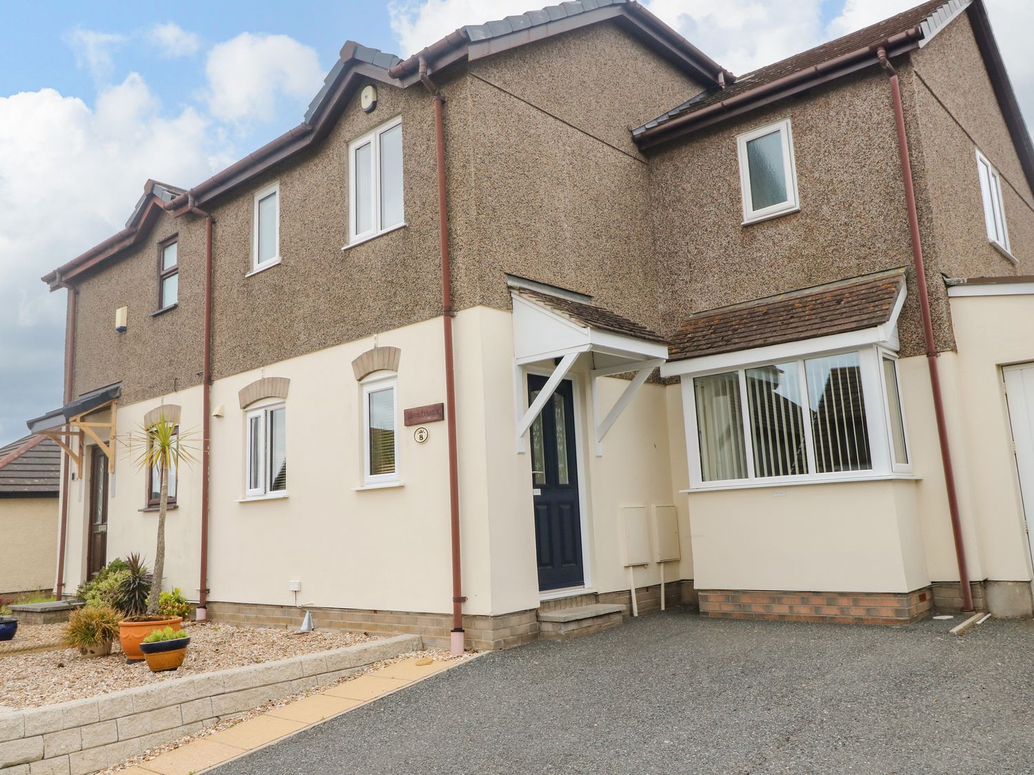 An exterior view of a two story house with a driveway and potted plants at Pentewan in Hayle