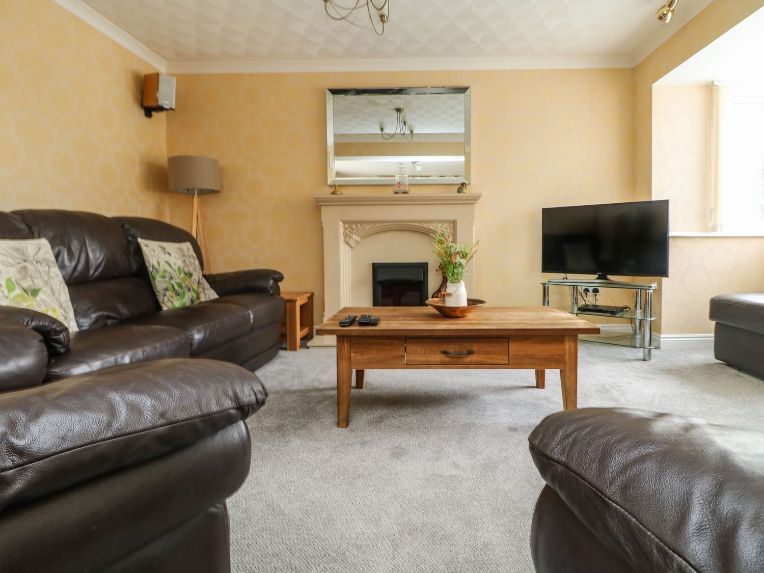 A living room with brown leather sofas a wooden coffee table a fireplace with a mirror above a TV on a glass stand and a floor lamp at Pentewan in Hayle