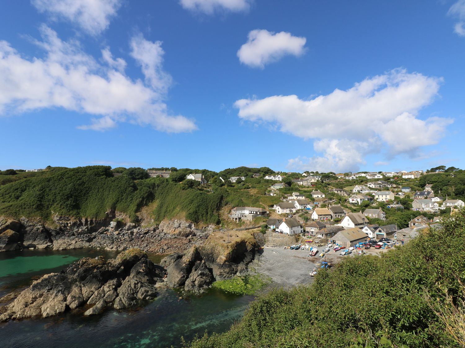 A coastal village with houses near rocky cliffs and green vegetation at Mengarth in Cadgwith