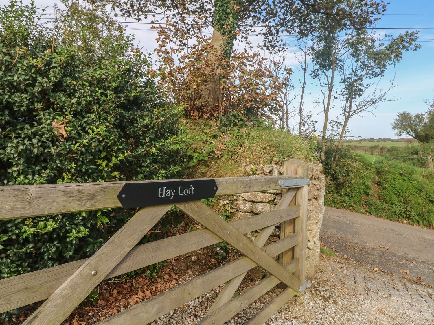 A wooden gate with a sign saying Hay Loft beside a gravel driveway and greenery at Hay Loft in Bolenowe Nr Portreath