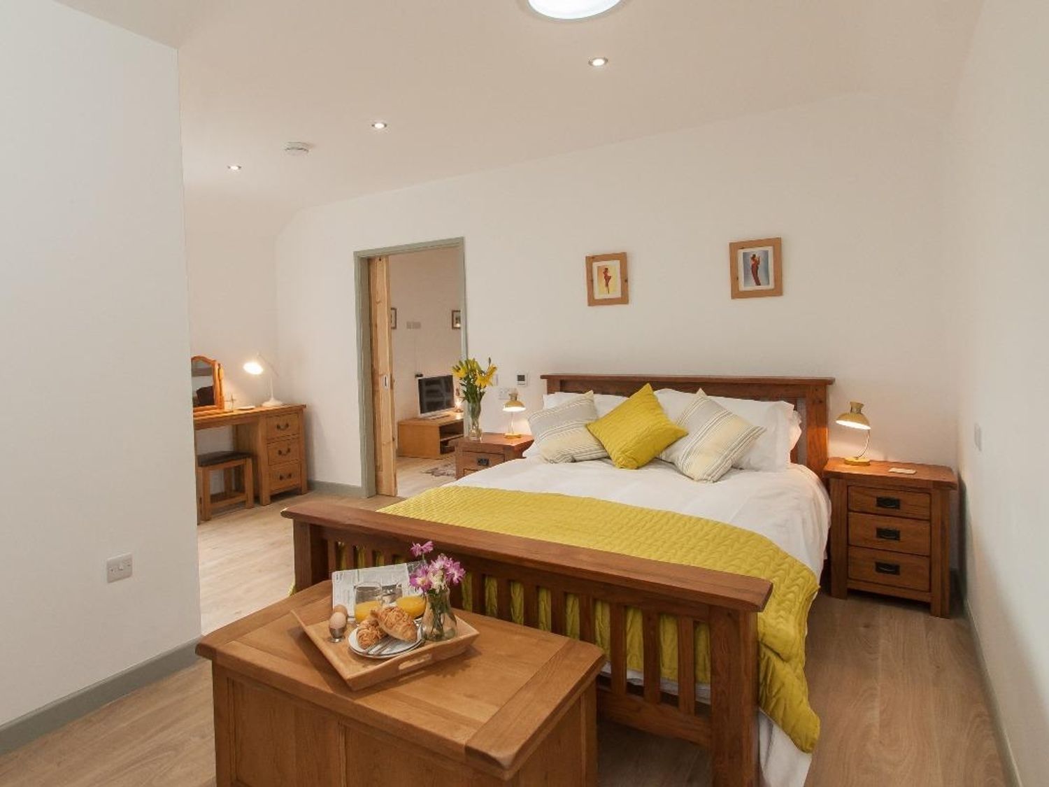 A bedroom with a wooden bed frame yellow bedding nightstands a dresser and a tray with breakfast at Fritillary Cottage in Bradworthy
