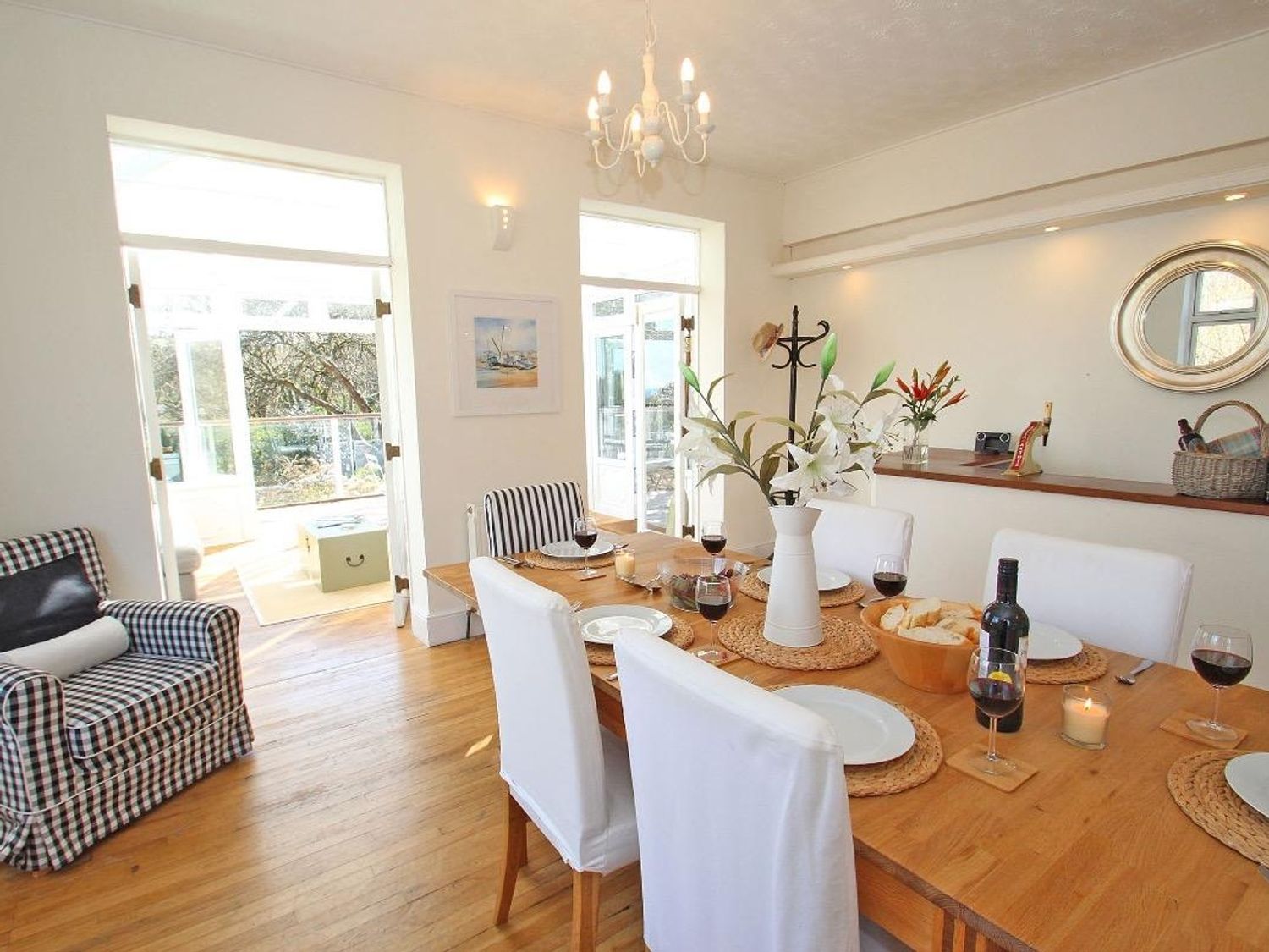 A dining room with a wooden table set with plates wine glasses and a vase of flowers at Porthcurno Bay View in Porthcurno
