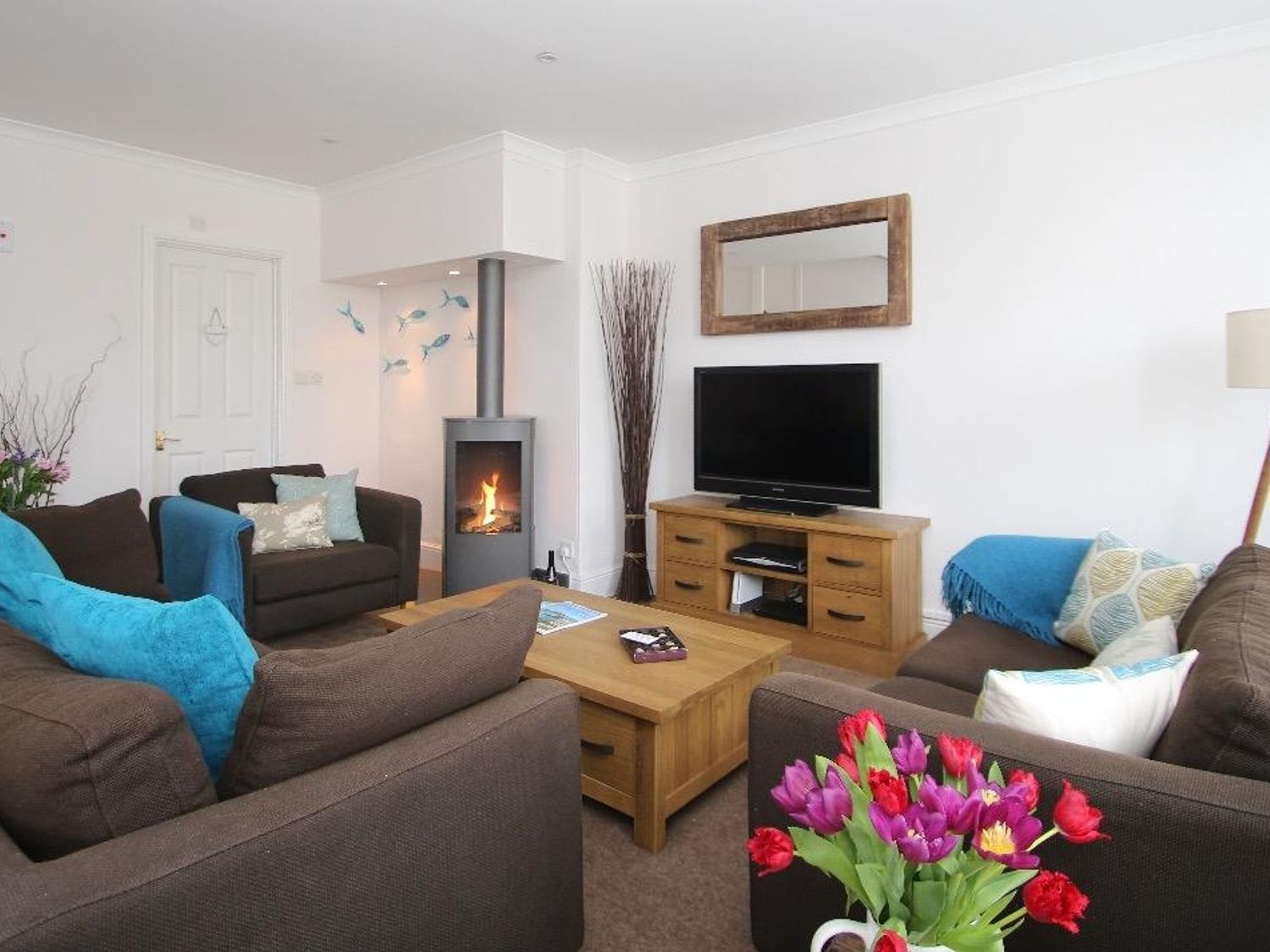 A living room with brown sofas a wooden coffee table a TV on a wooden stand a fireplace and flowers on a table at Porthcurno Bay View in Porthcurno