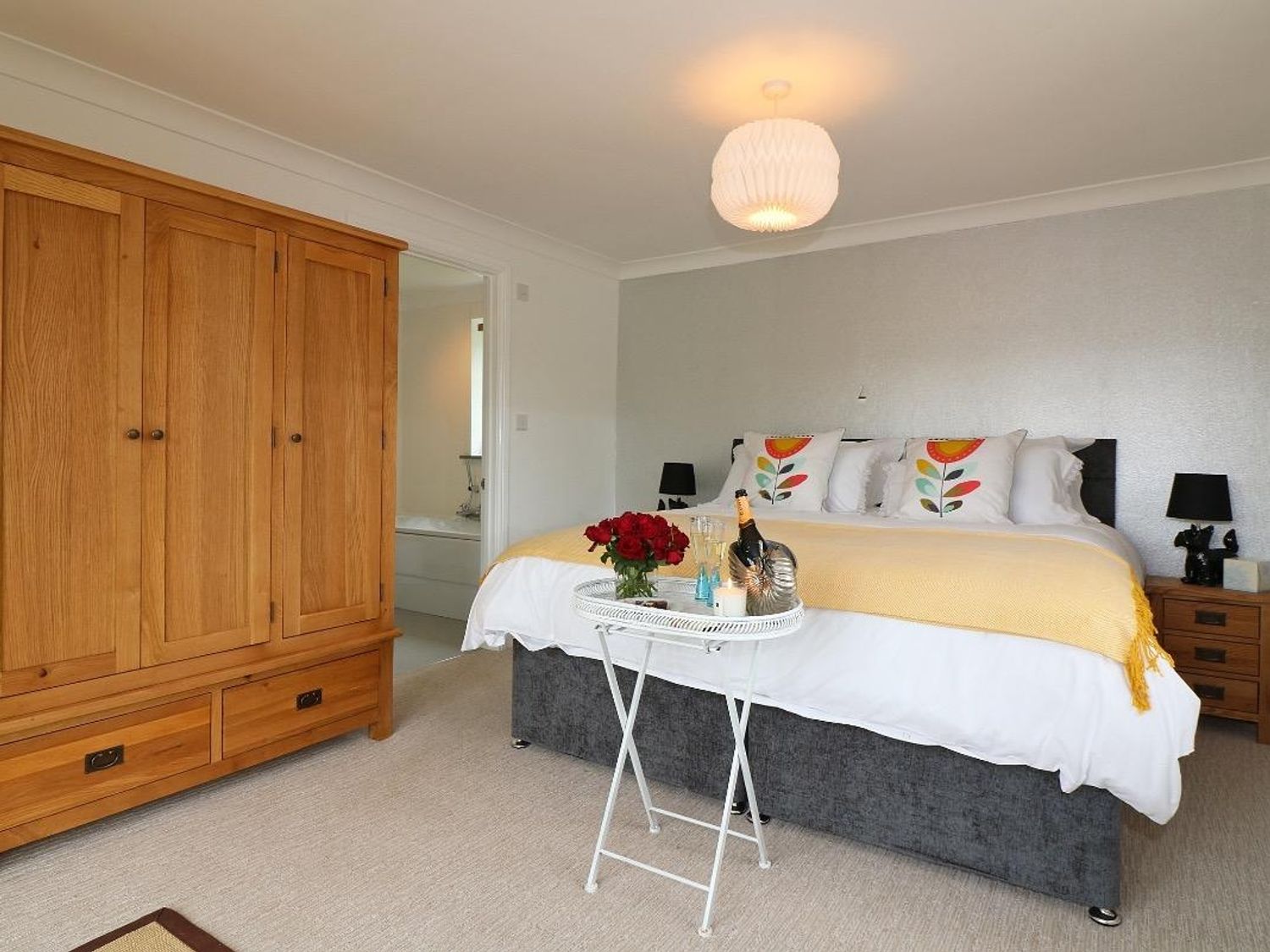 A bedroom with a double bed with pillows and yellow throw and a wooden wardrobe with bedside tables at Omalast Chacewater near Truro