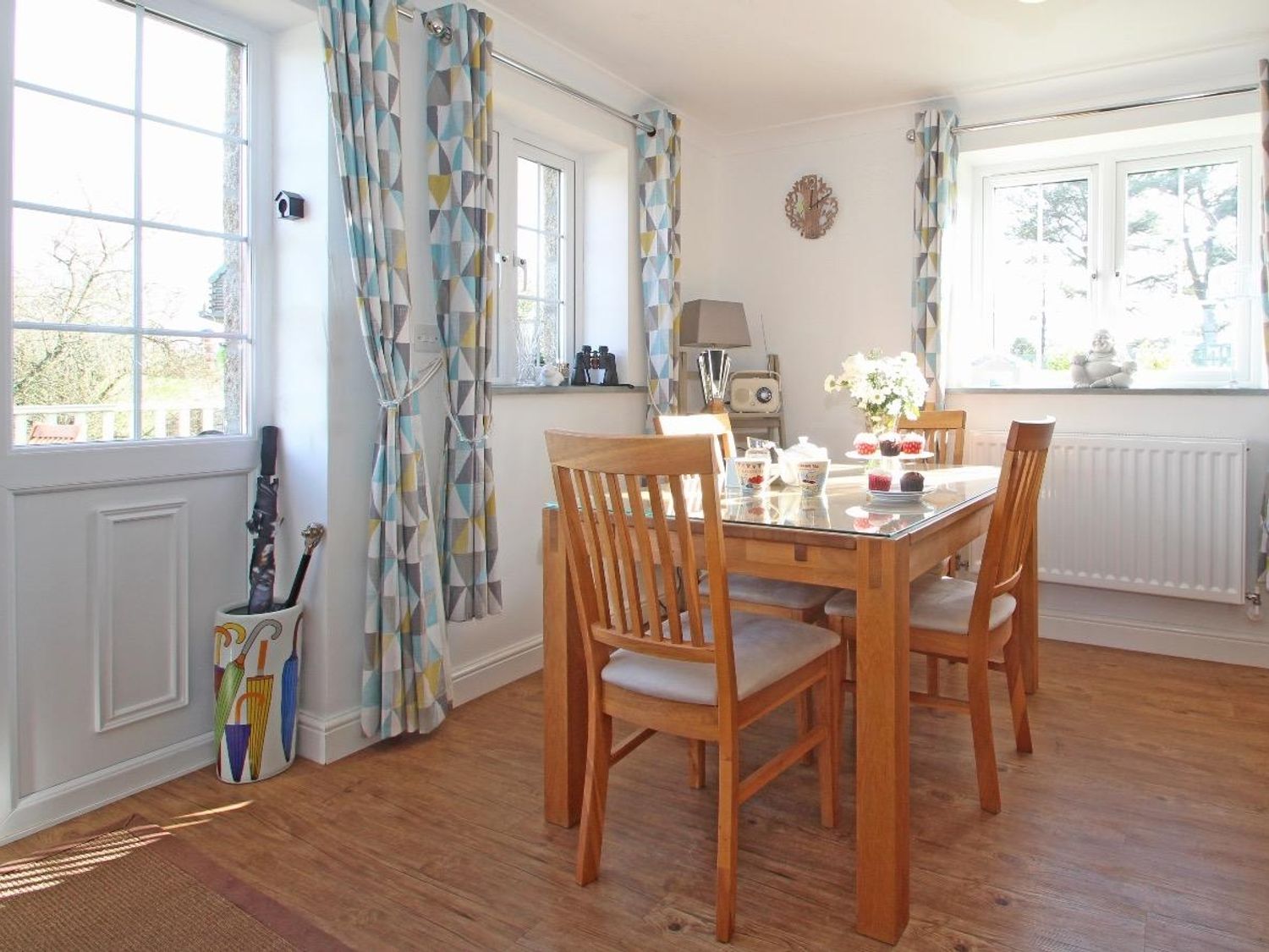 A dining room with a wooden table and four chairs near windows with patterned curtains at Omalast in Chacewater near Truro