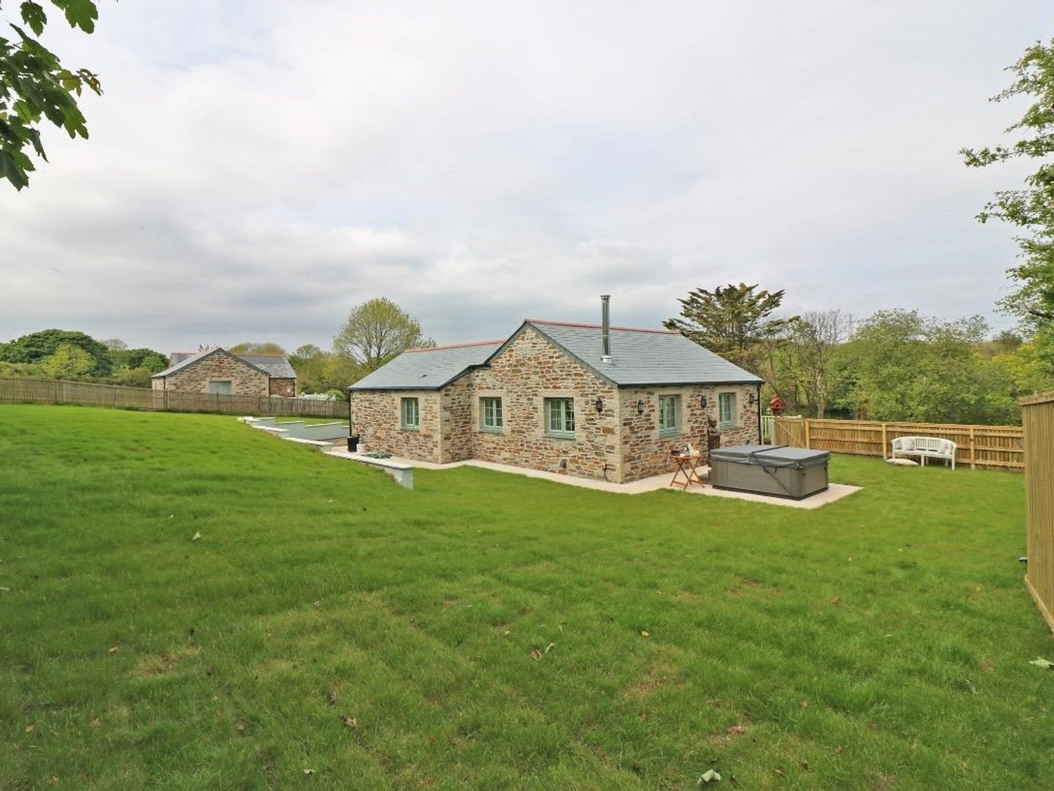 A stone cottage with a fenced grassy yard hot tub and outdoor seating at Omalast in Chacewater near Truro