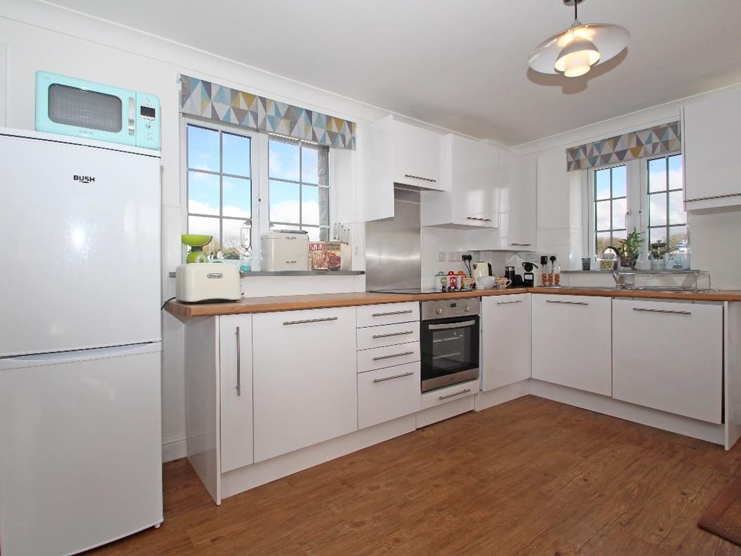 A kitchen with white cabinets wooden countertops and two windows with patterned valances at Omalast Chacewater near Truro
