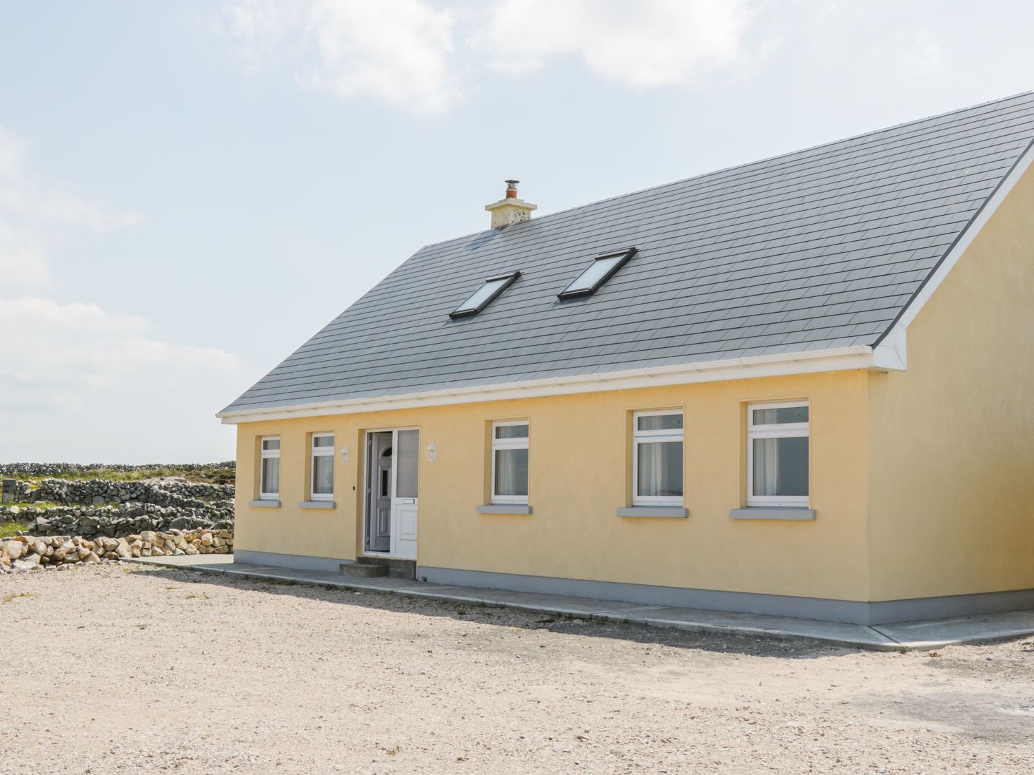 A yellow single-story house with gray roof skylights and a white door in a rural area at Lakeview in Lettermore County Galway
