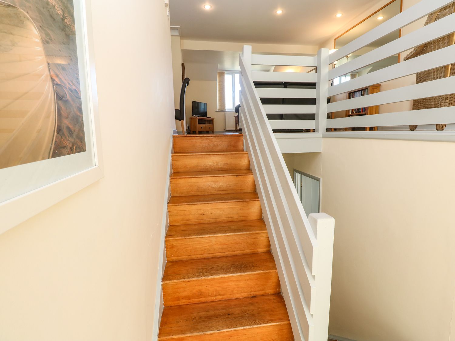 A wooden staircase with white railing leading to a room with a chair and television at Atlantic Edge in Newquay