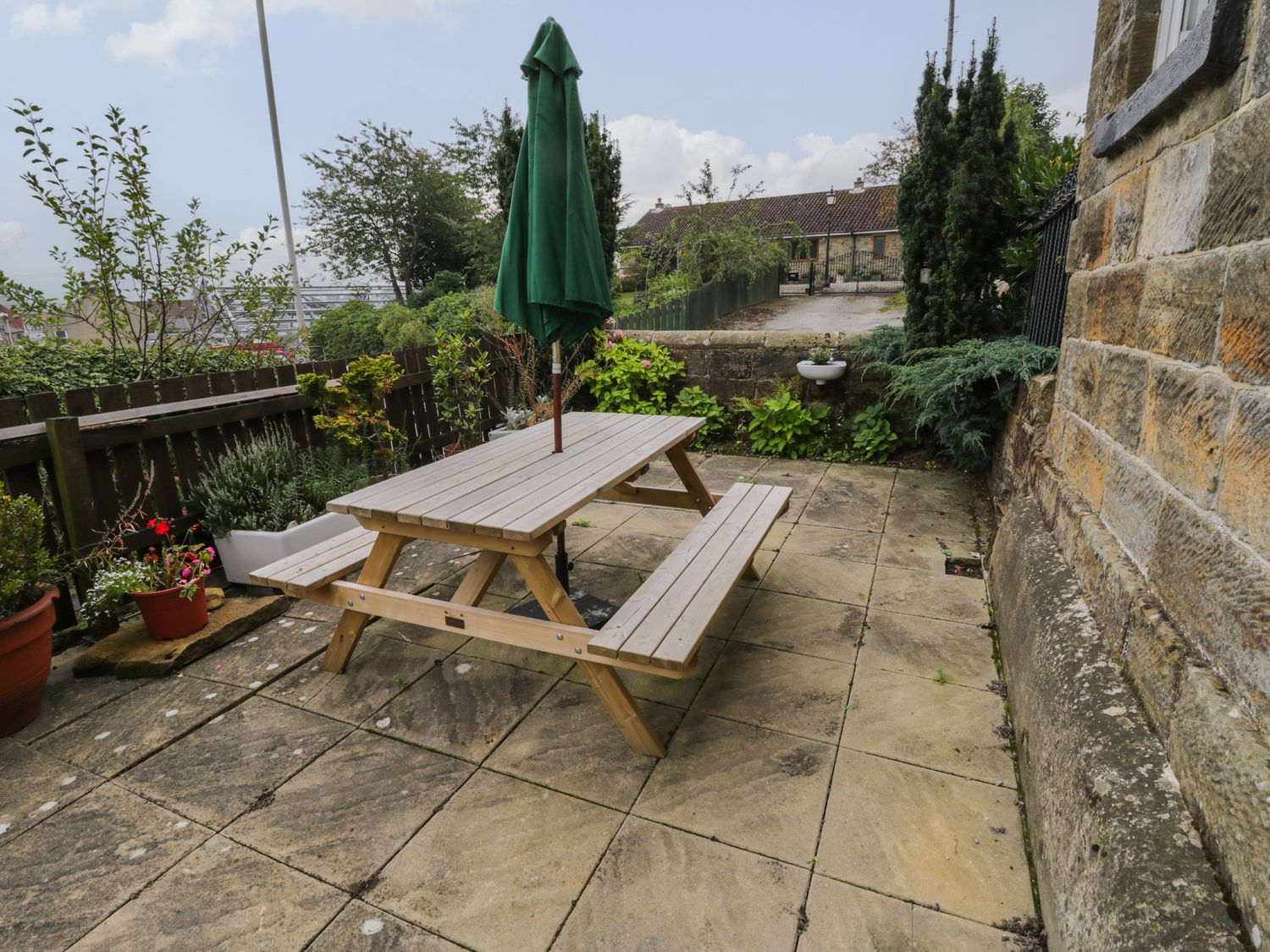 An outdoor patio with a wooden picnic table and green umbrella next to a stone wall at Springfield Cottage in Castleton