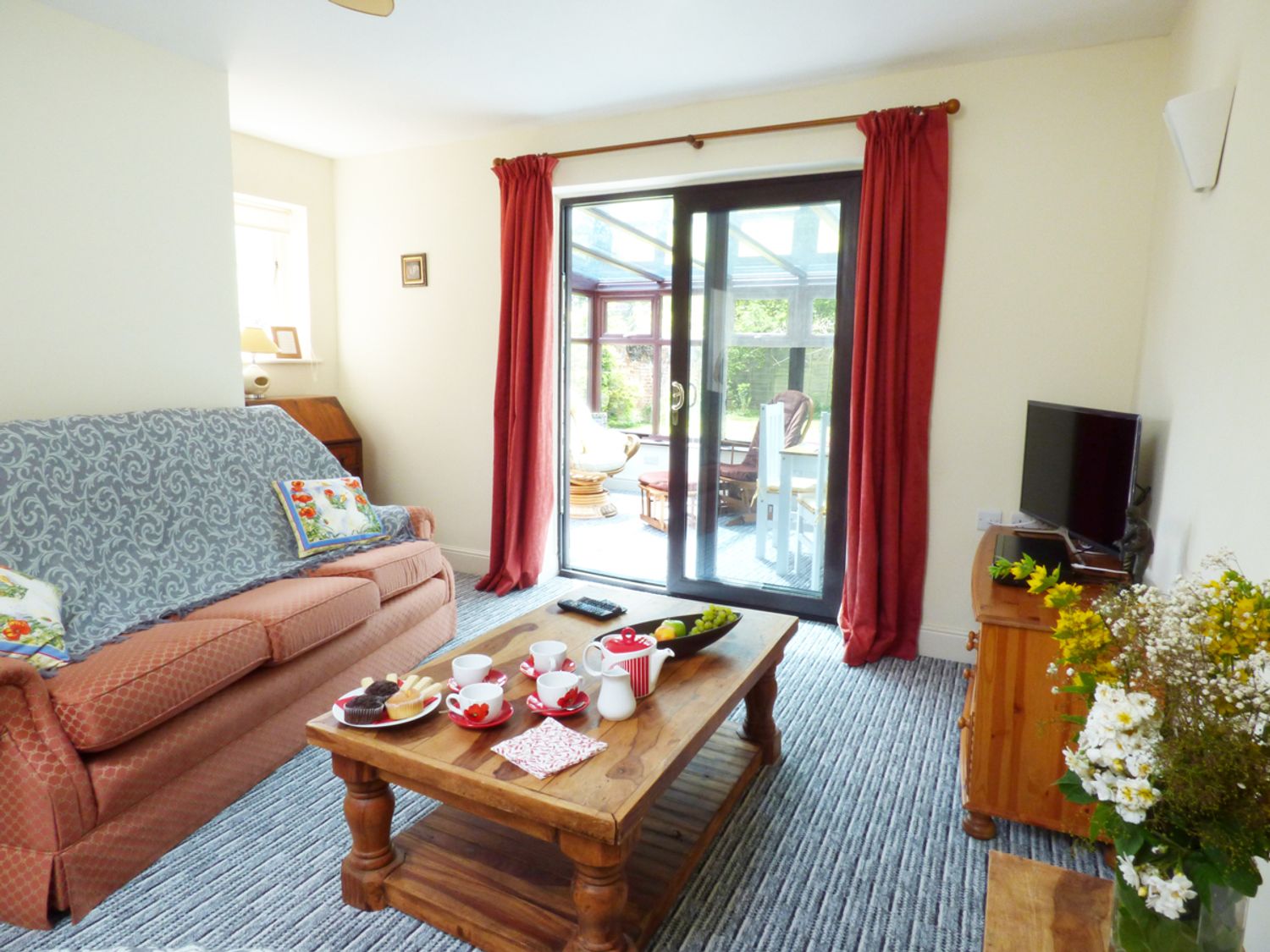 A living room with a sofa tea set on a wooden table and sliding glass doors with red curtains at 27 Swan Street in Boxford