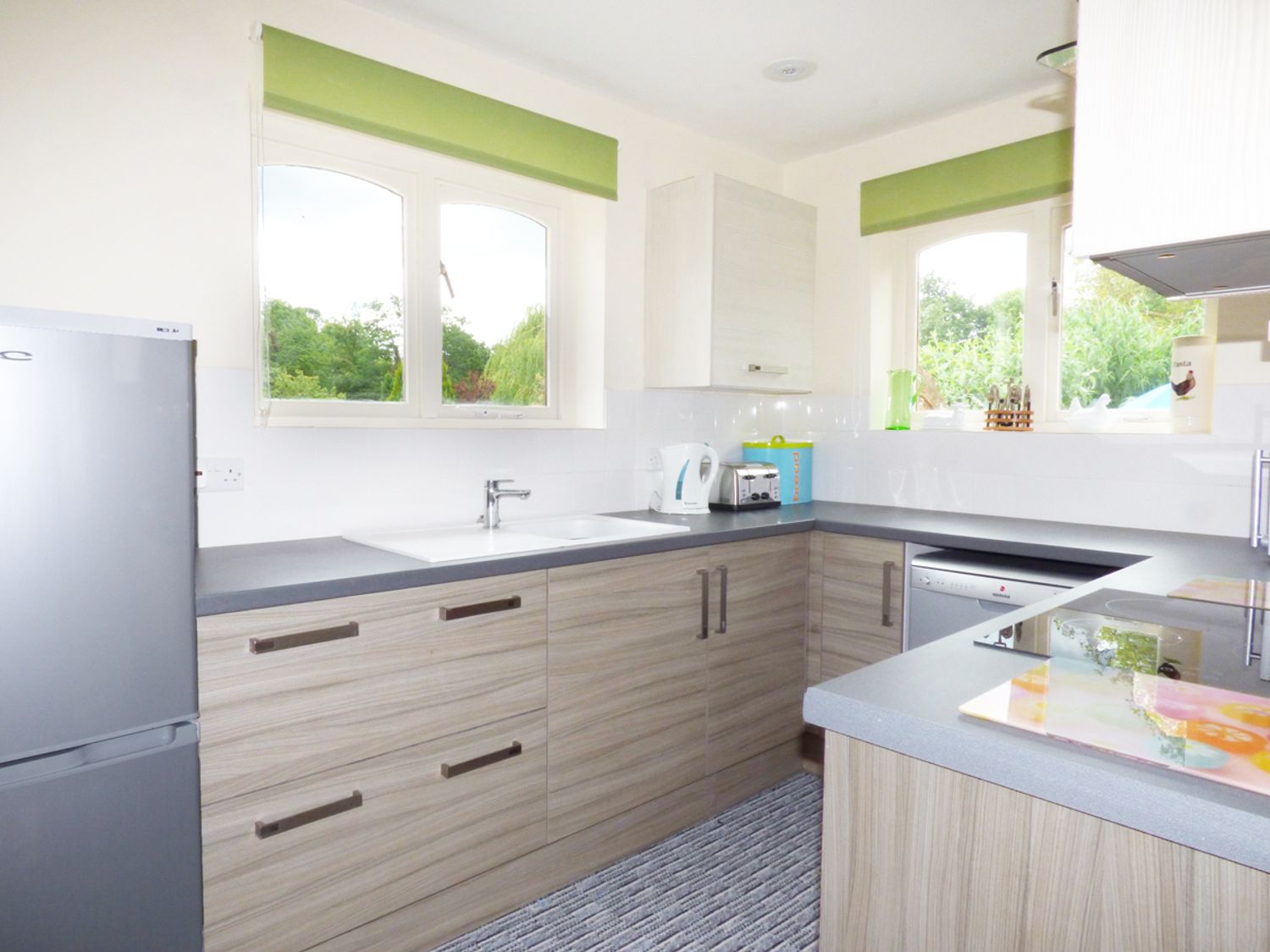 A kitchen with wooden cabinets a stainless steel fridge a double sink a kettle toaster and a dishwasher at 27 Swan Street Boxford