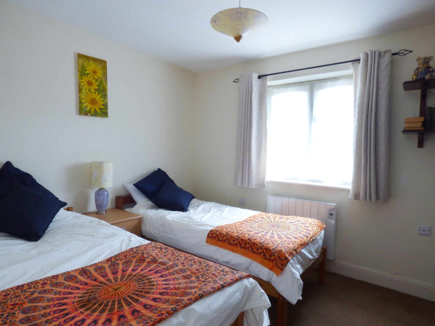 A bedroom with two single beds white bedding and orange patterned throws at 27 Swan Street in Boxford