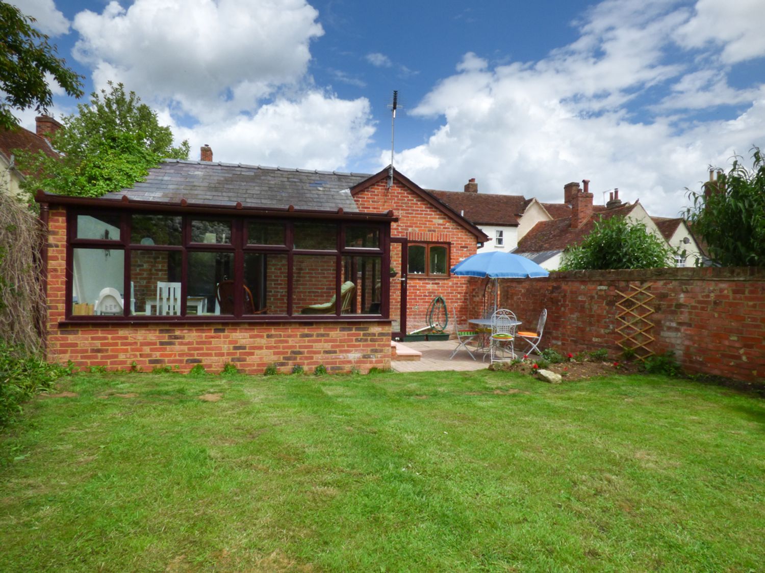 A backyard with a lawn and a brick patio area with a table and chairs under a blue umbrella at 27 Swan Street in Boxford