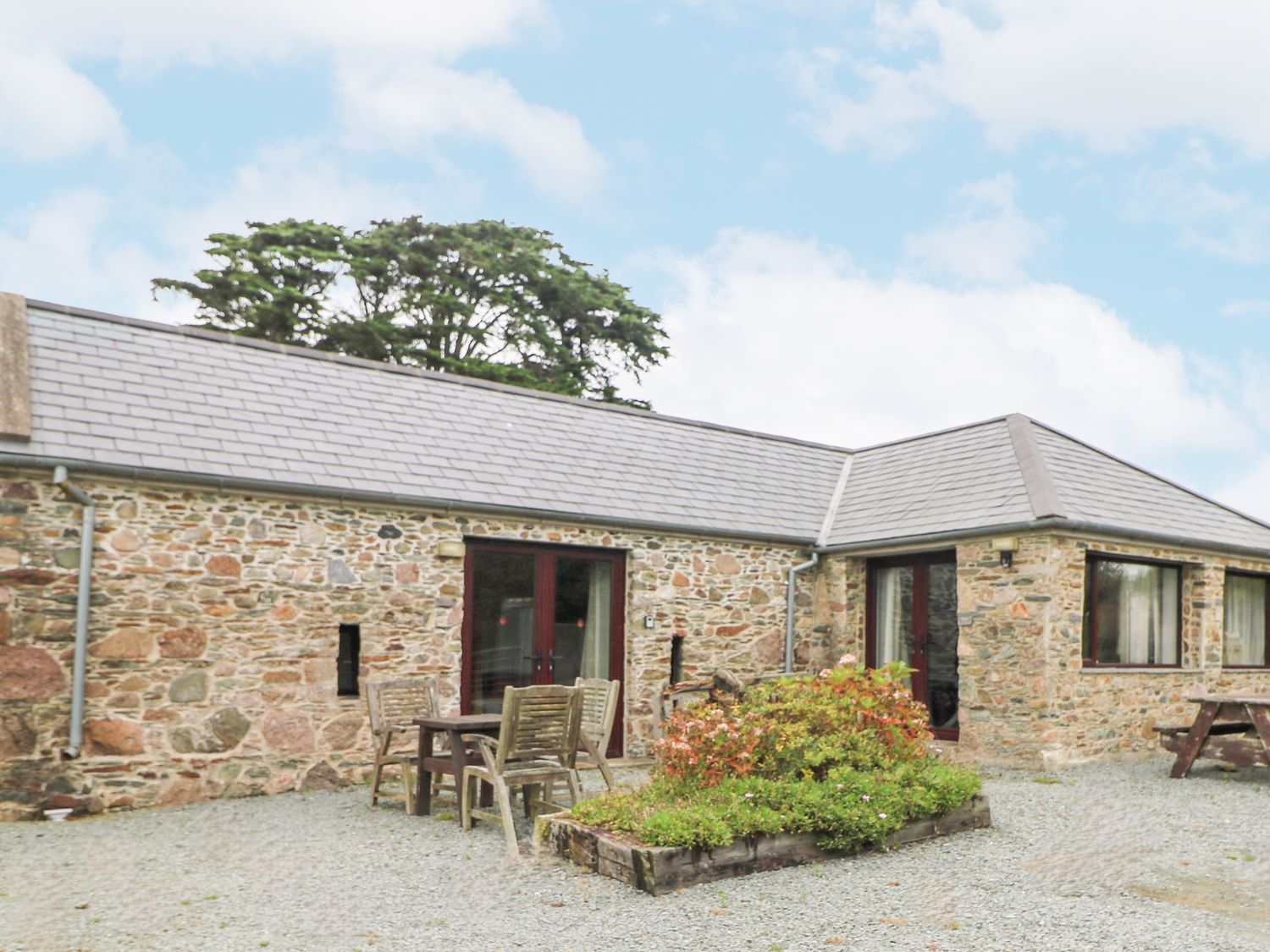 An outdoor area with a stone house a wooden table and chairs and a flower bed at Swallow's Nest in Tacumshane County Wexford