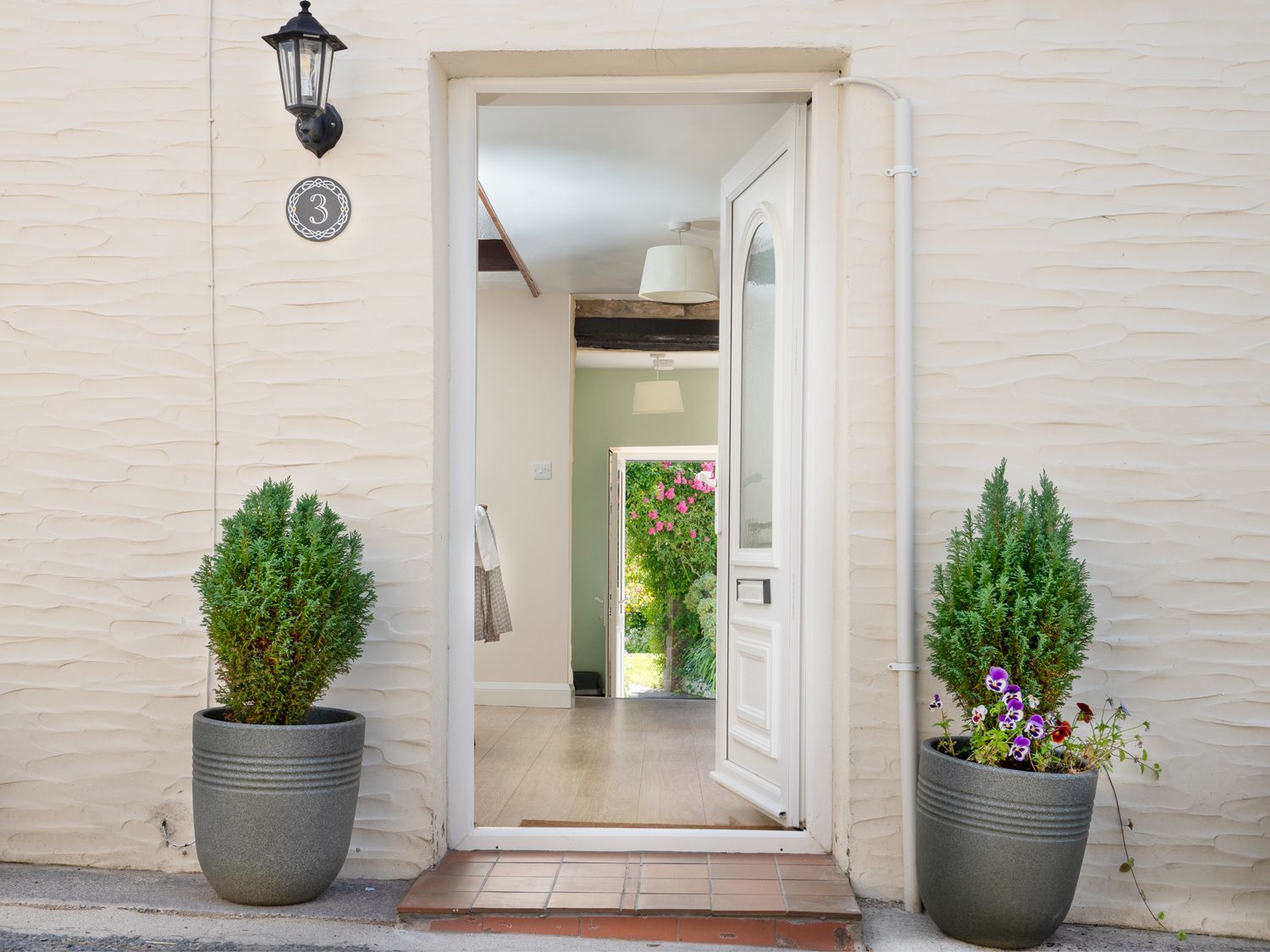 Open front door with two potted plants outside and a hallway leading to a garden at 3 Horse Pool Road in Laugharne