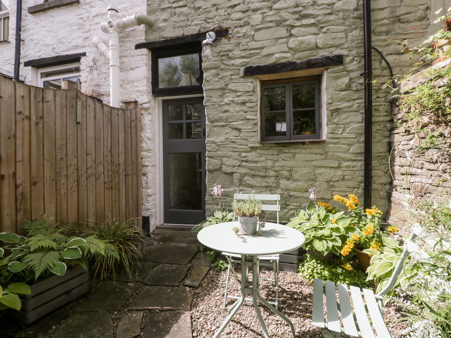 A small outdoor patio with a round table and two chairs surrounded by plants and a stone wall at 7 Bell Street in Talgarth
