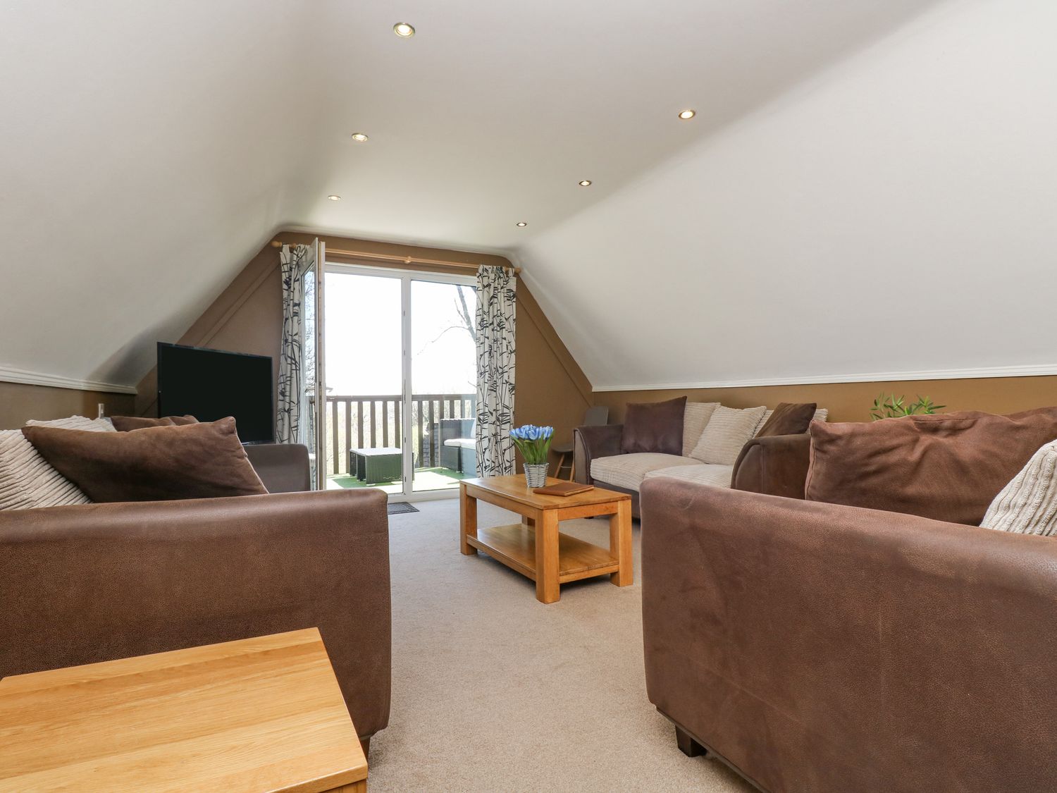 A living room with sofas coffee table and television near balcony doors at Valley Lodge 61 in Callington