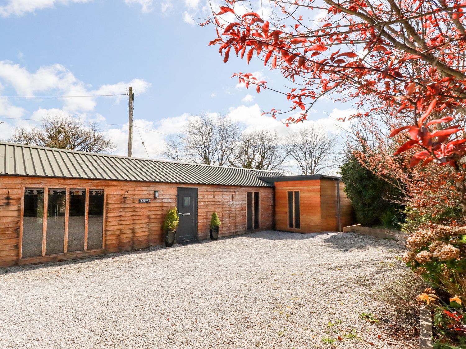 A single-story wooden building with a gravel driveway and plants at Kelyow in St Day