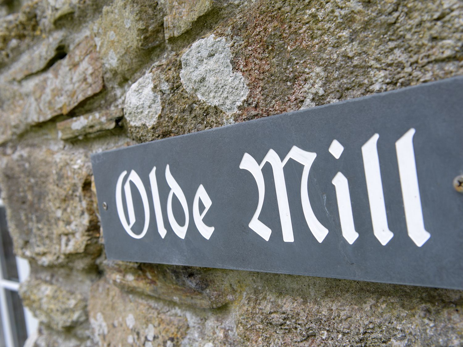 A stone wall with a metal sign reading Olde Mill at Old Mill Cottage in Camelford