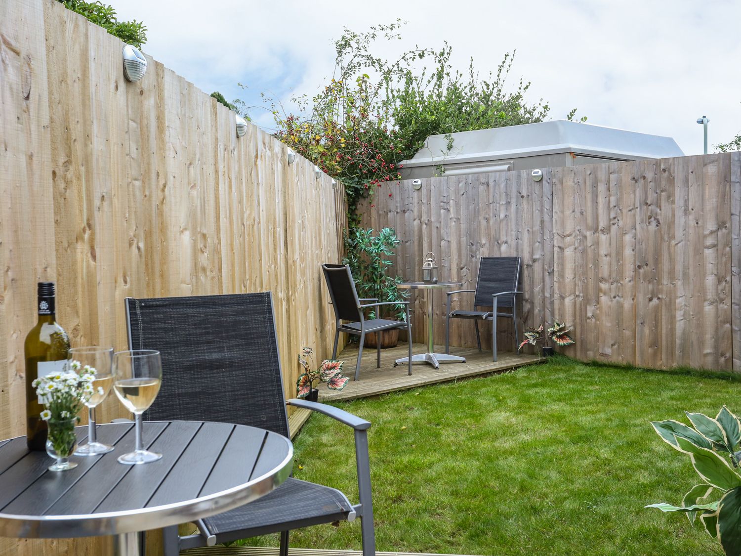 A small fenced garden with two tables and four chairs on grass at The Cabin in Combe Martin