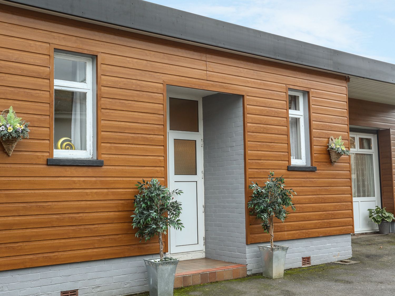 An exterior view of a building with wooden siding two windows a door and potted plants at The Cabin in Combe Martin