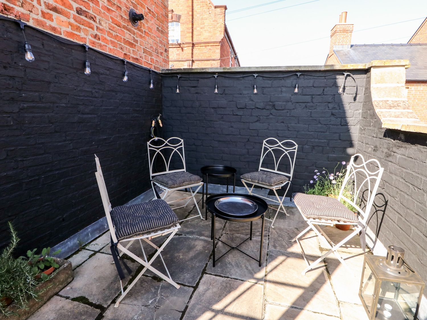 An outdoor patio with four metal chairs with cushions two small round tables string lights and potted plants at 12 Banks Street in Horncastle