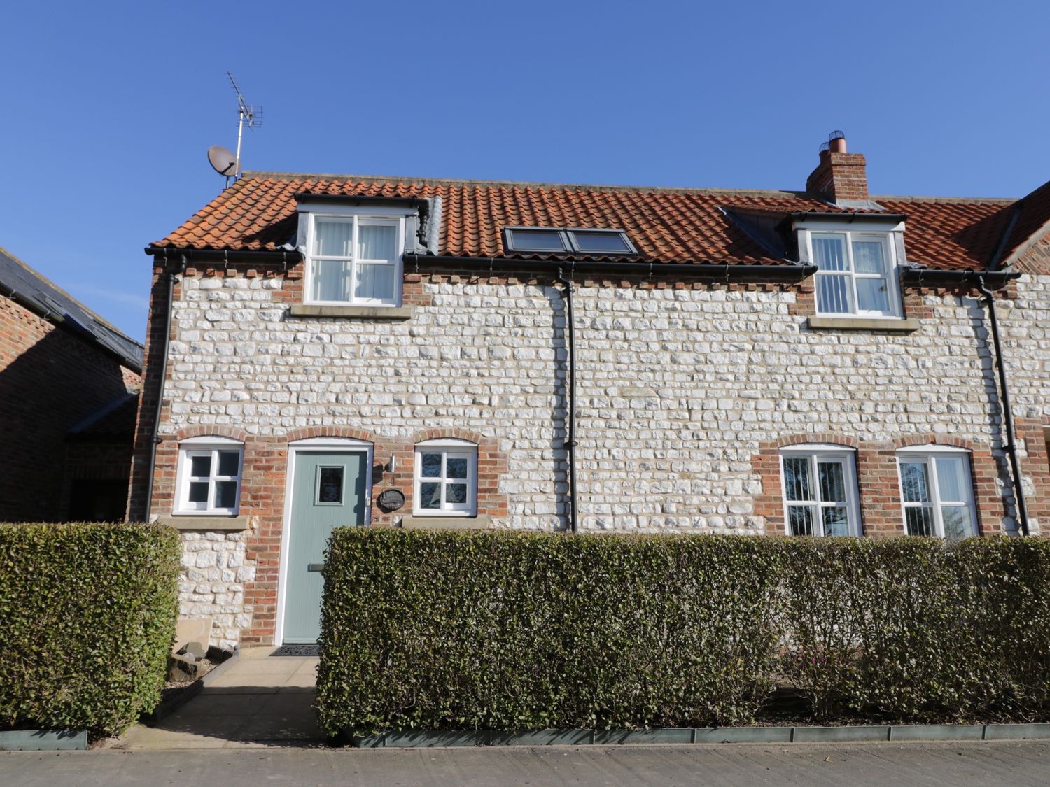 A stone cottage with a green door and windows behind a trimmed hedge at Pebble Cottage Dunnscroft in Flamborough