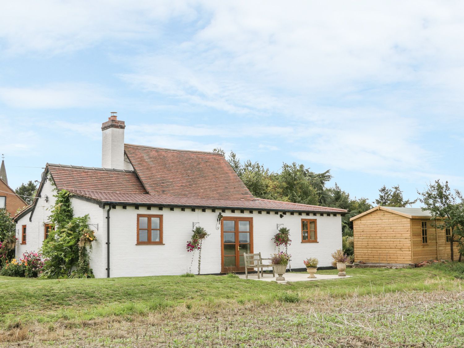 A white house with a tiled roof and chimney next to a wooden shed and a grassy yard at Little Pound House in Mamble