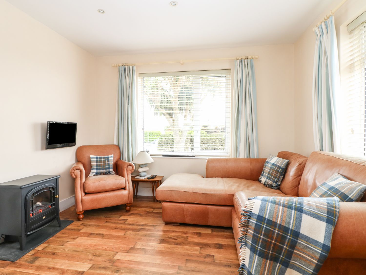 A living room with a leather sofa armchair side table lamp a wall-mounted TV and a heater at Bolenowe Trebetherick near Polzeath