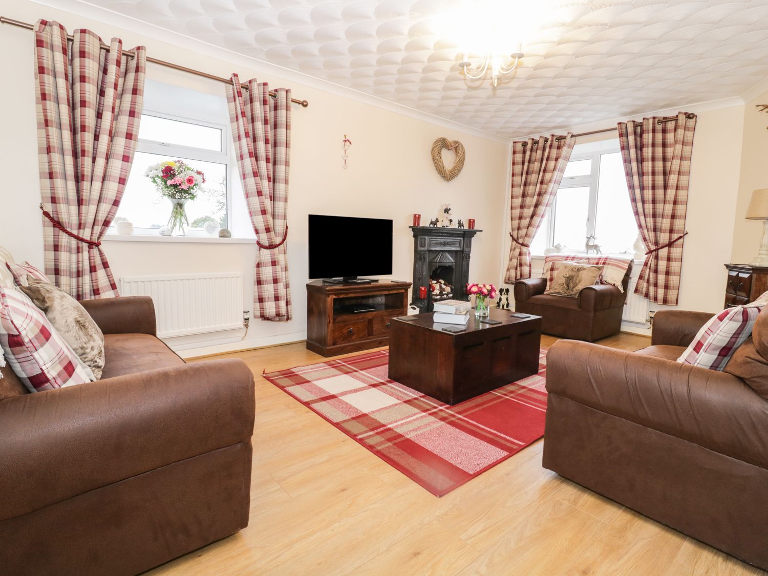 A living room with brown sofas red plaid curtains and a dark wooden coffee table at Tyn Y Gorlan in Criccieth