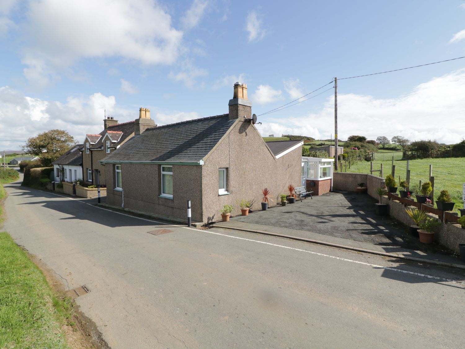 A row of houses along a country road with potted plants and a bench outside a house at Trigfa Cottage in Abersoch