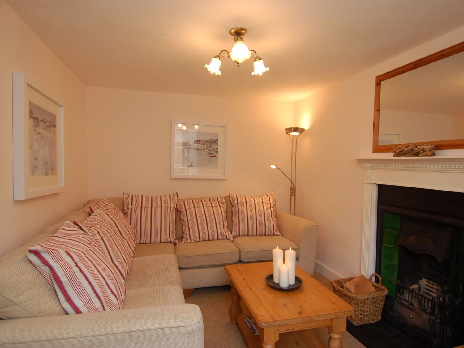 A living room with a beige sofa striped cushions wooden coffee table candles fireplace and framed pictures at Jordan House Boscastle